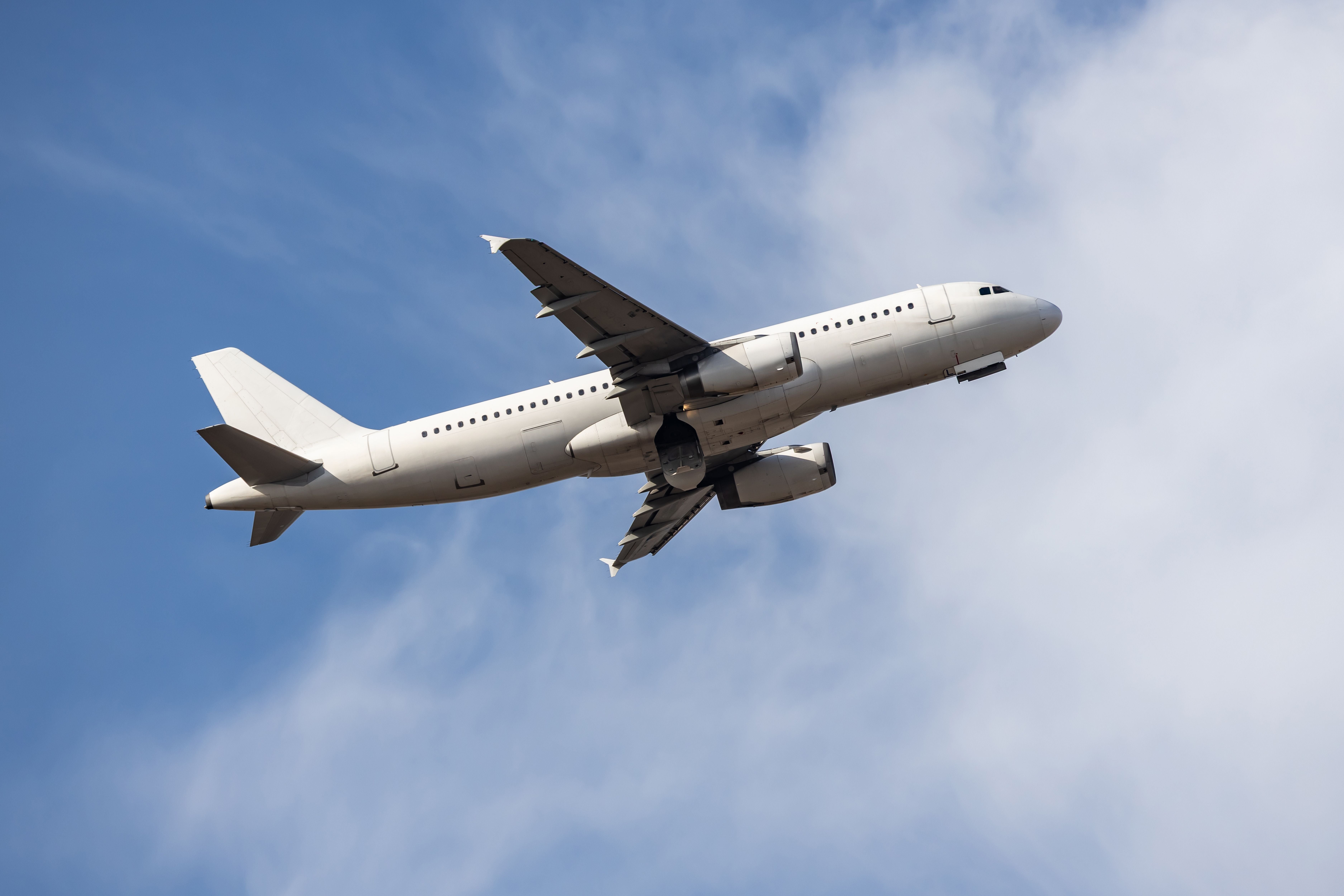 Weißes Passagierflugzeug fliegt am blauen Himmel mit leichten Wolken.
