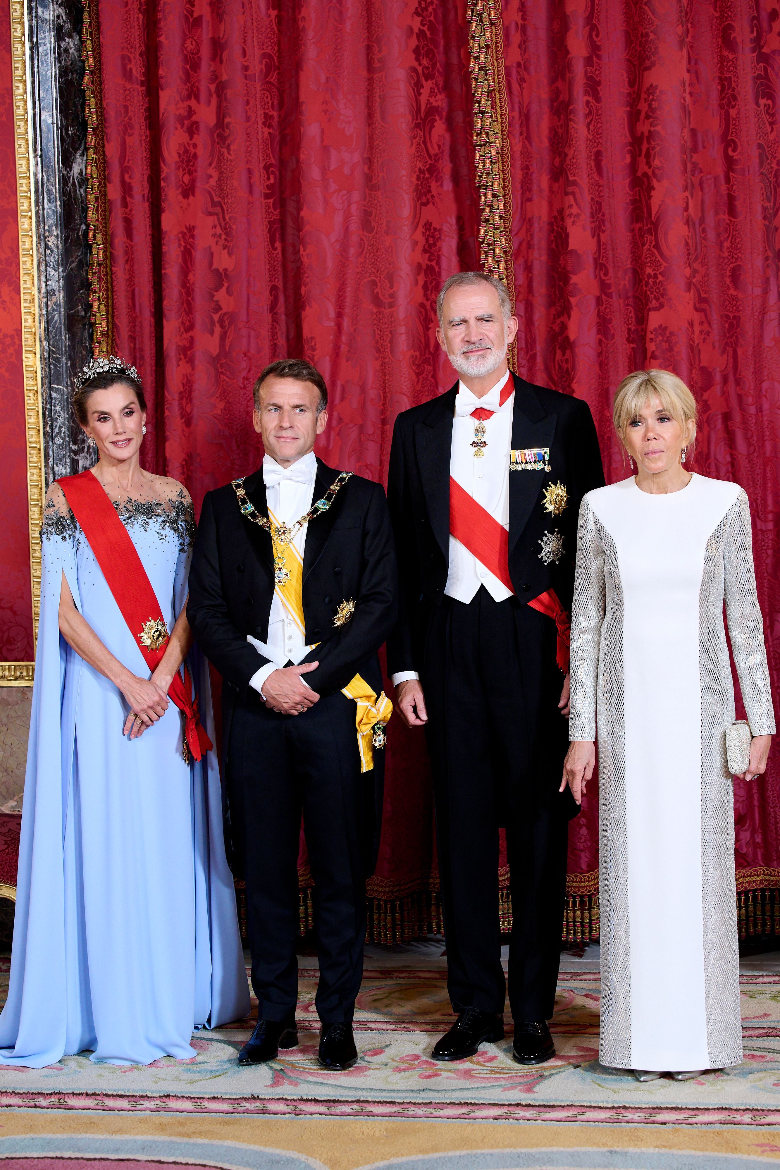 Vier elegant gekleidete Personen posieren vor rotem Vorhang im königlichen Palast von Madrid.