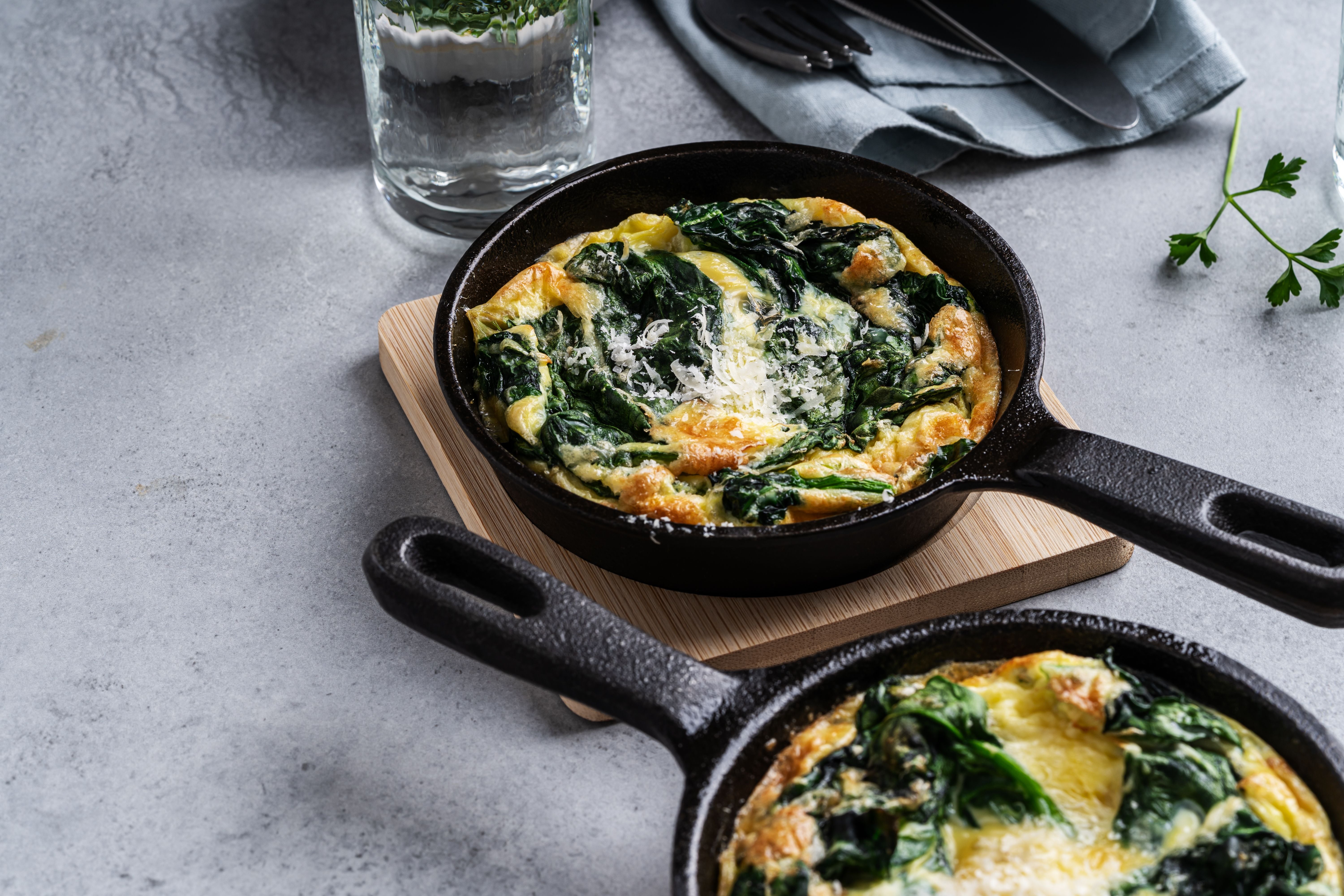 Spinat-Frittata in einer gusseisernen Pfanne auf einem grauen Frühstückstisch.