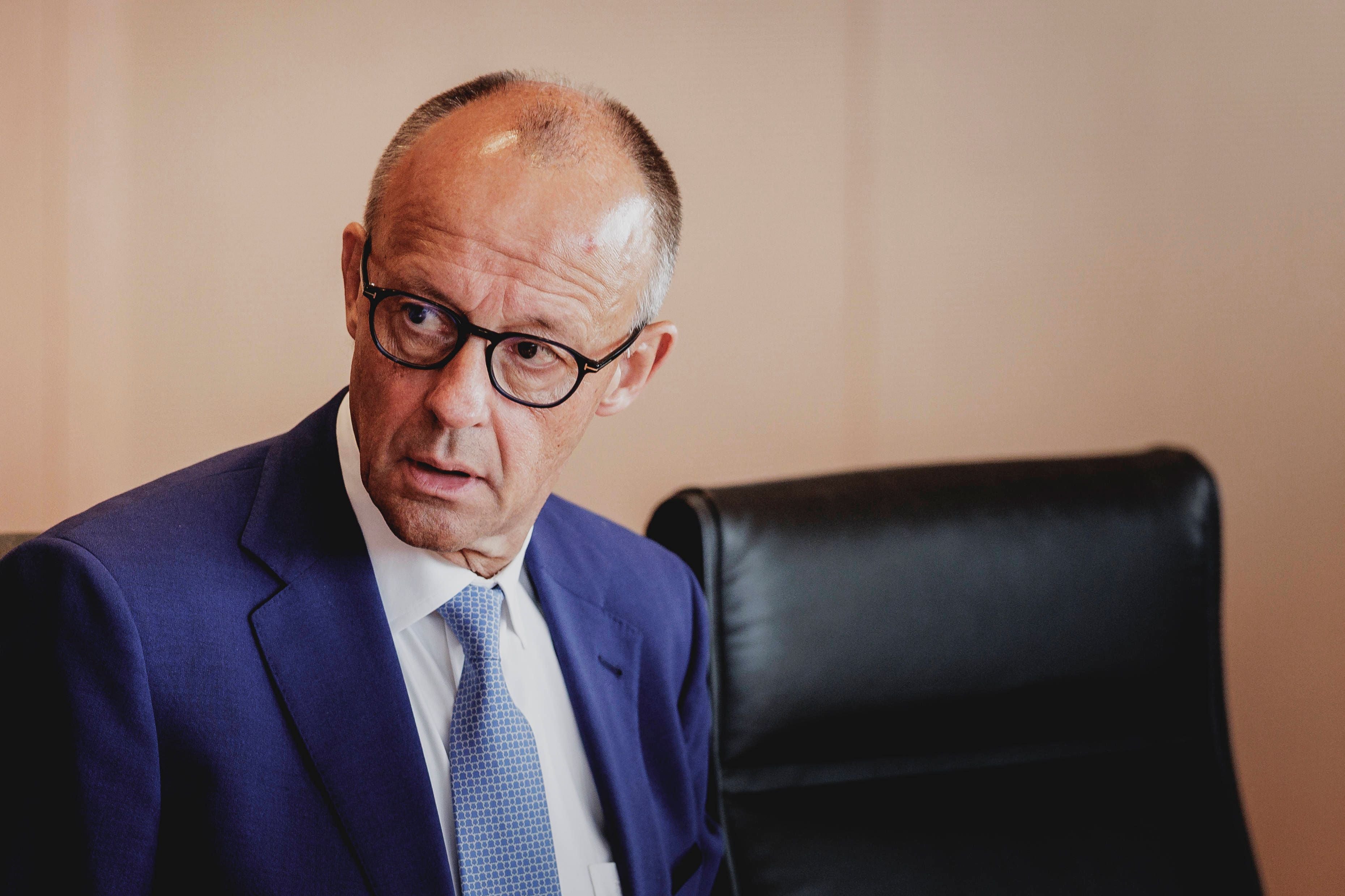 Ein Mann im blauen Anzug und mit Brille sitzt auf einem schwarzen Stuhl und schaut zur Seite.