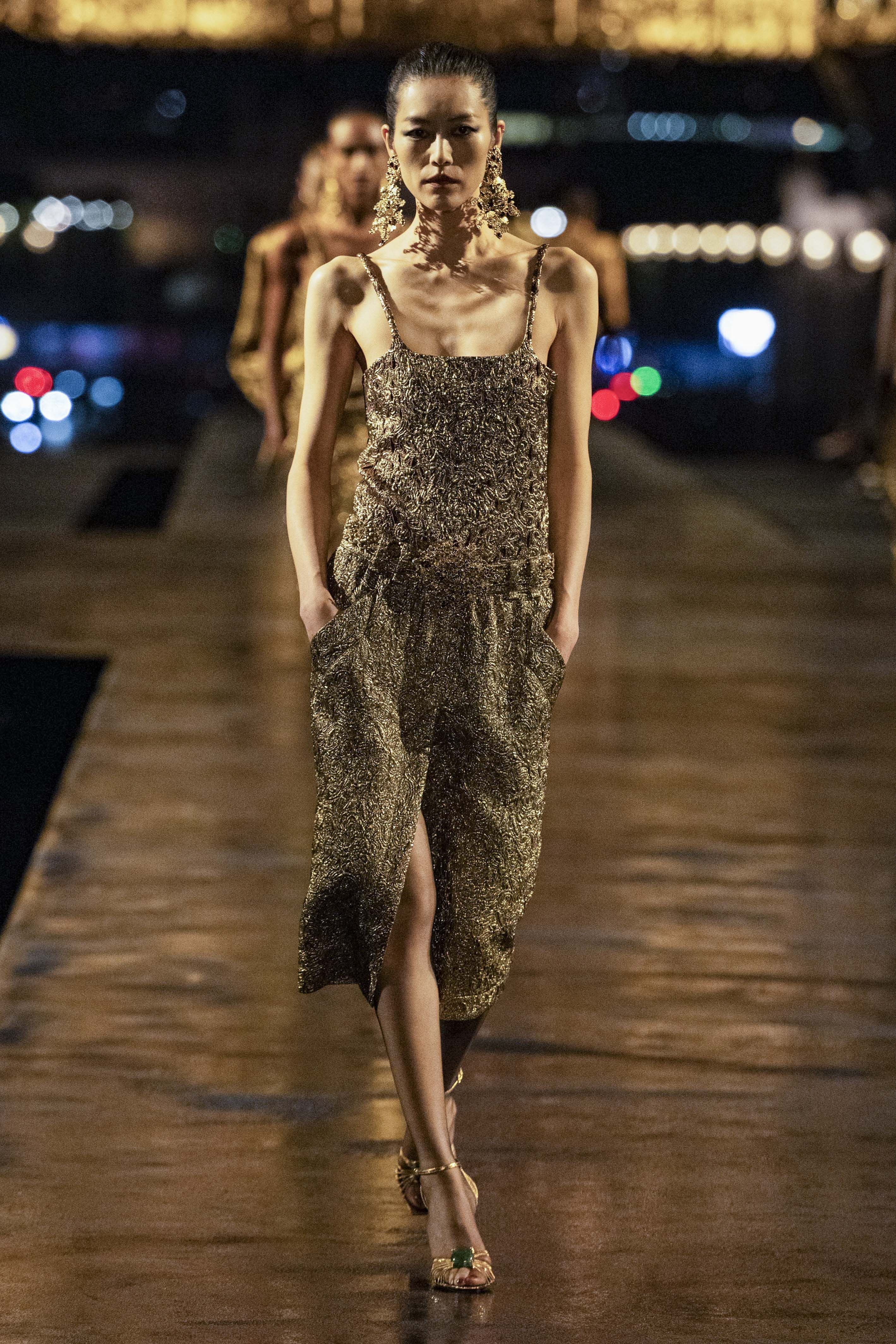 Model in golden Kleid und großen Ohrringen auf dem Laufsteg bei einer Modenschau.