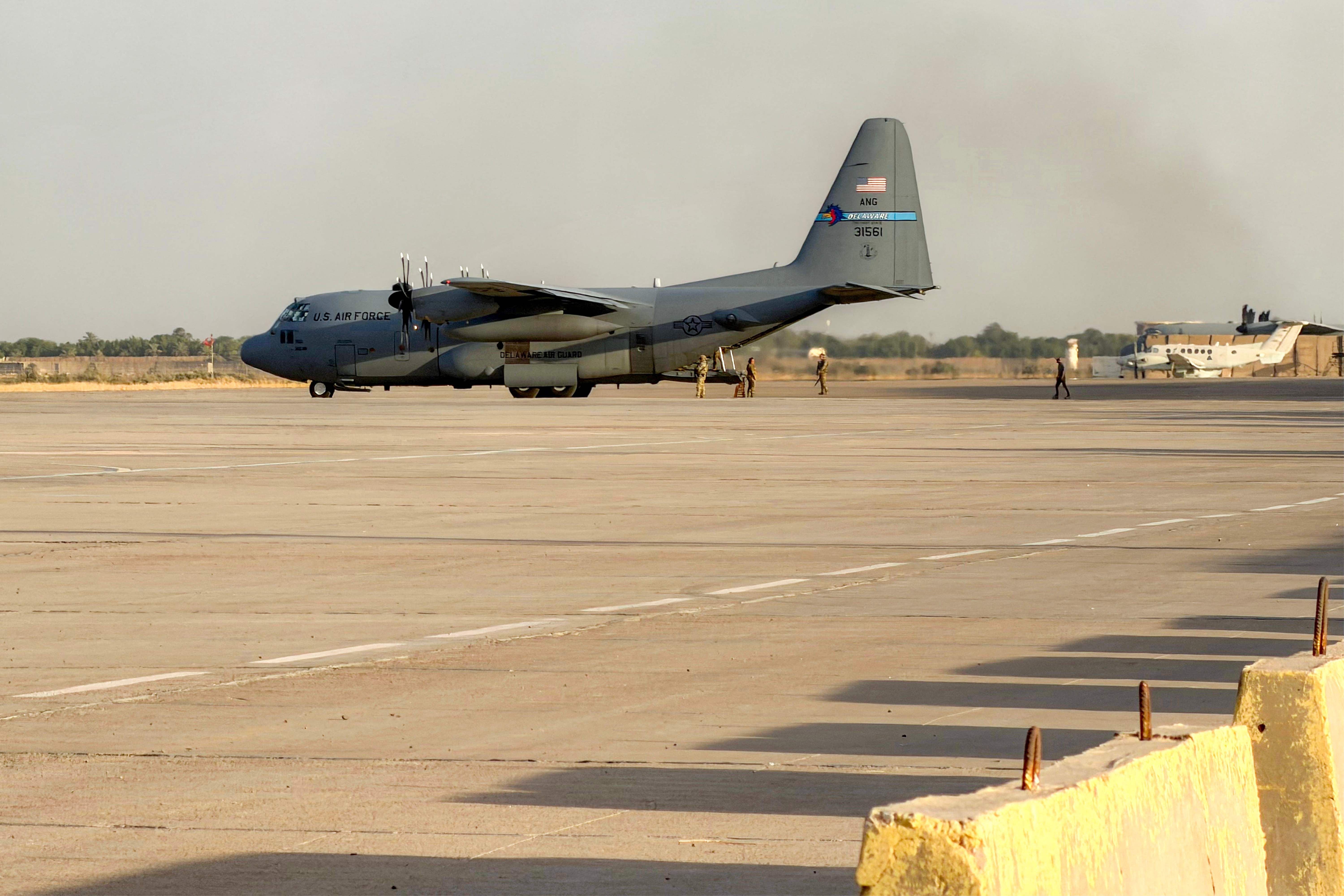Ein Transportflugzeug der US Air Force C-130 Hercules steht auf einer Startbahn mit Soldaten in der Nähe.