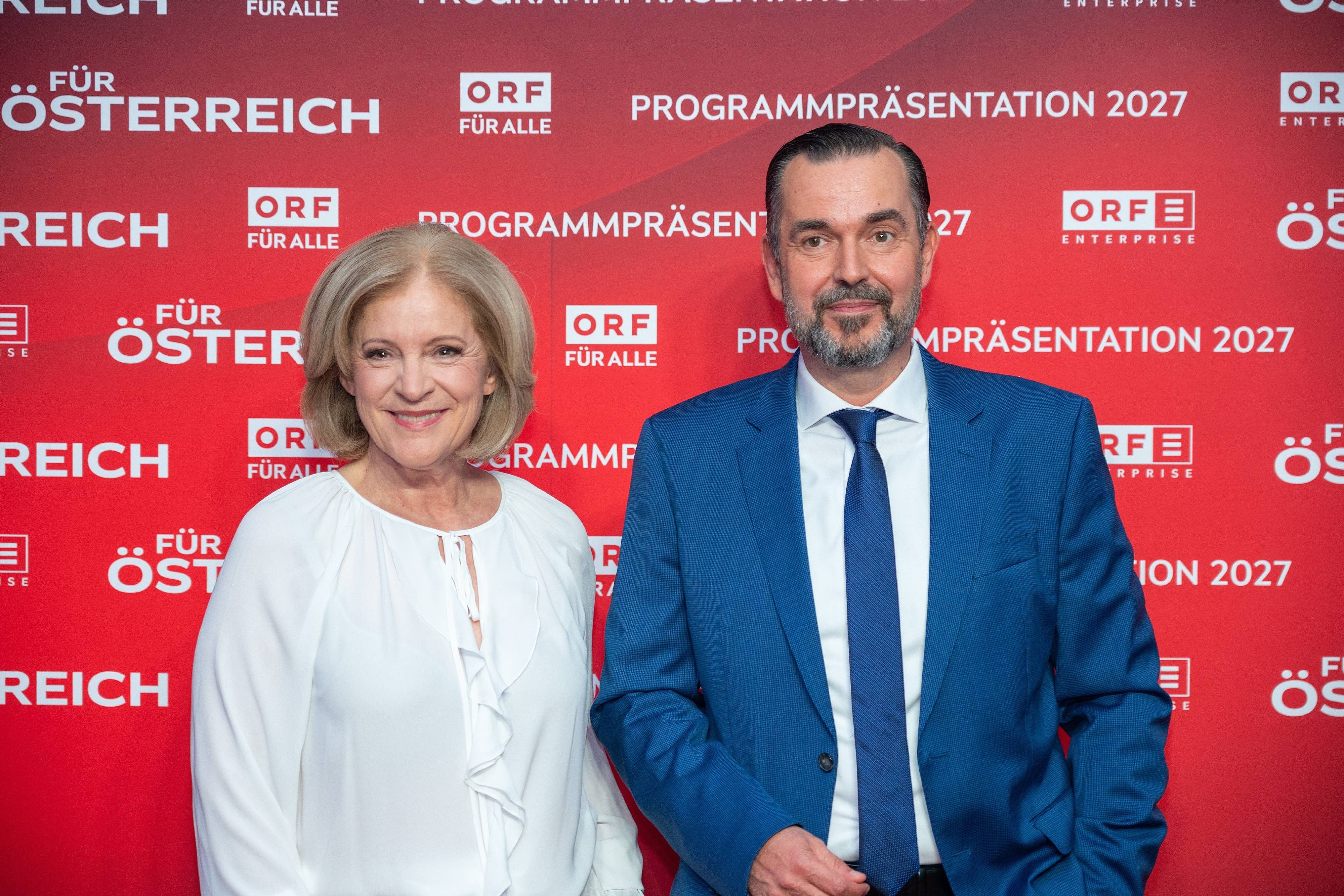 Eine Frau in Weiß und ein Mann im blauen Anzug vor rotem ORF-Programmpräsentations-Hintergrund.