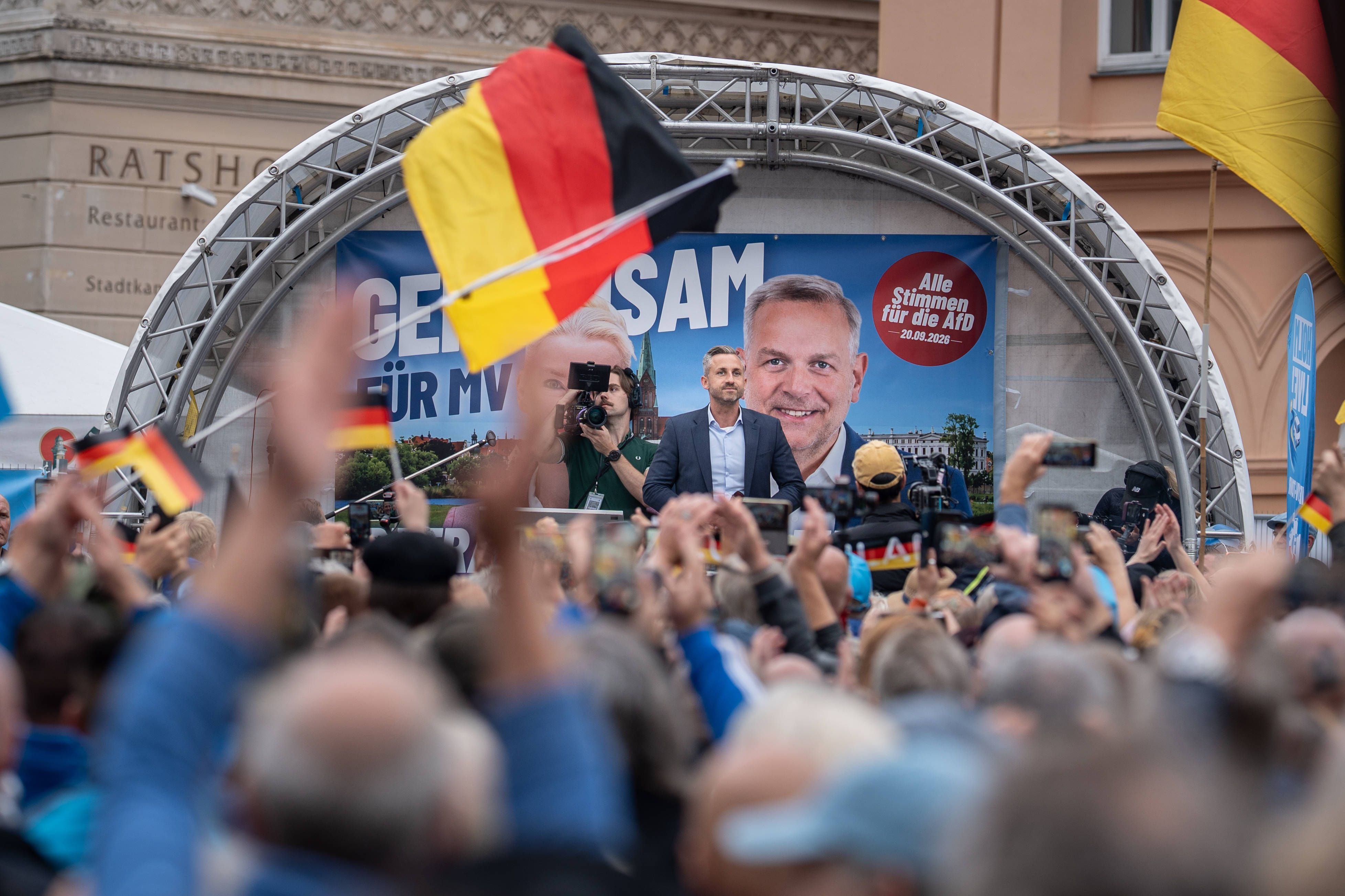 AfD-Wahlkampfveranstaltung mit vielen Menschen und Deutschlandflaggen vor einer Bühne mit Redner.