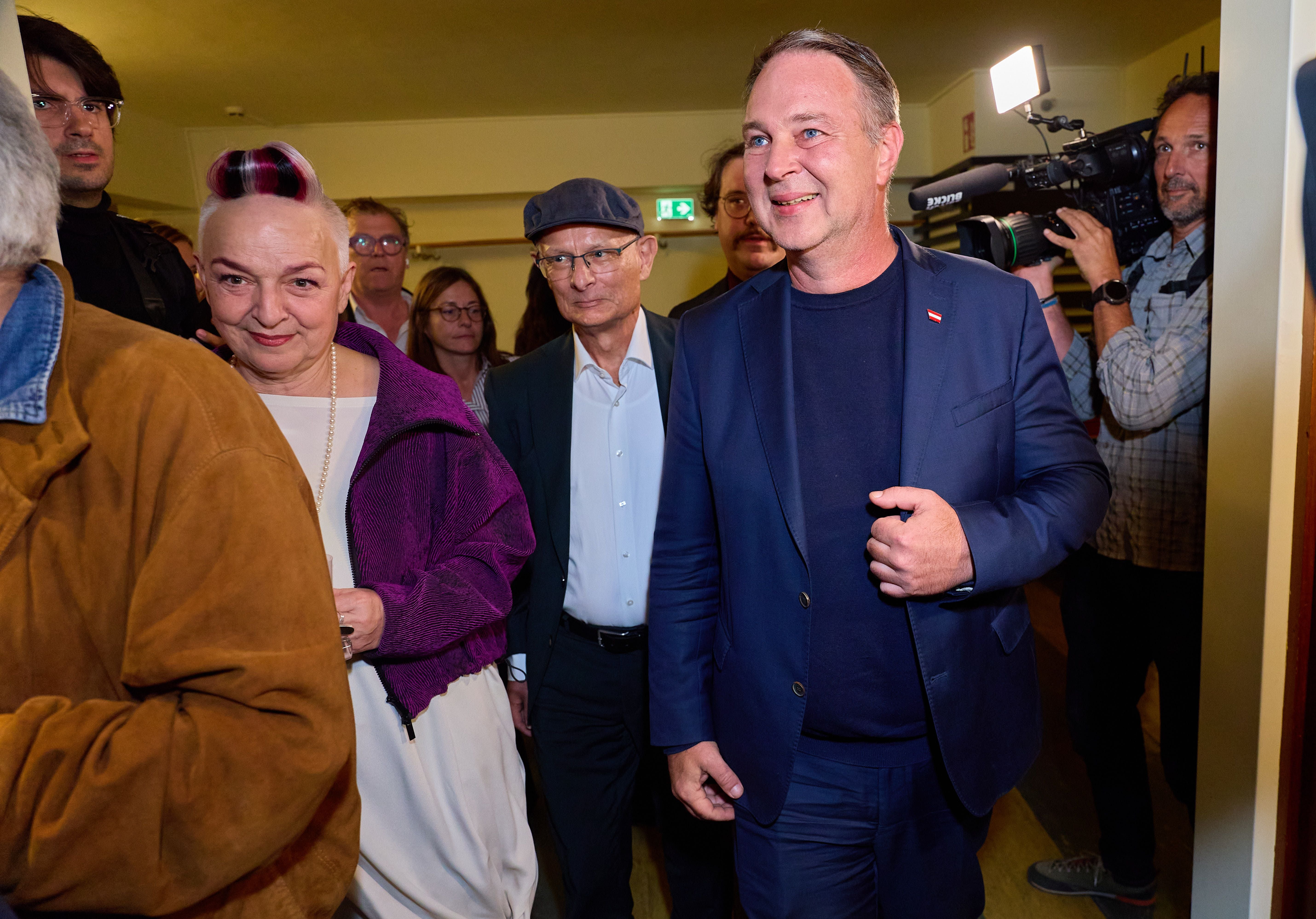 Mehrere Personen gehen lachend durch einen Flur, im Hintergrund ein Kameramann beim Filmen.