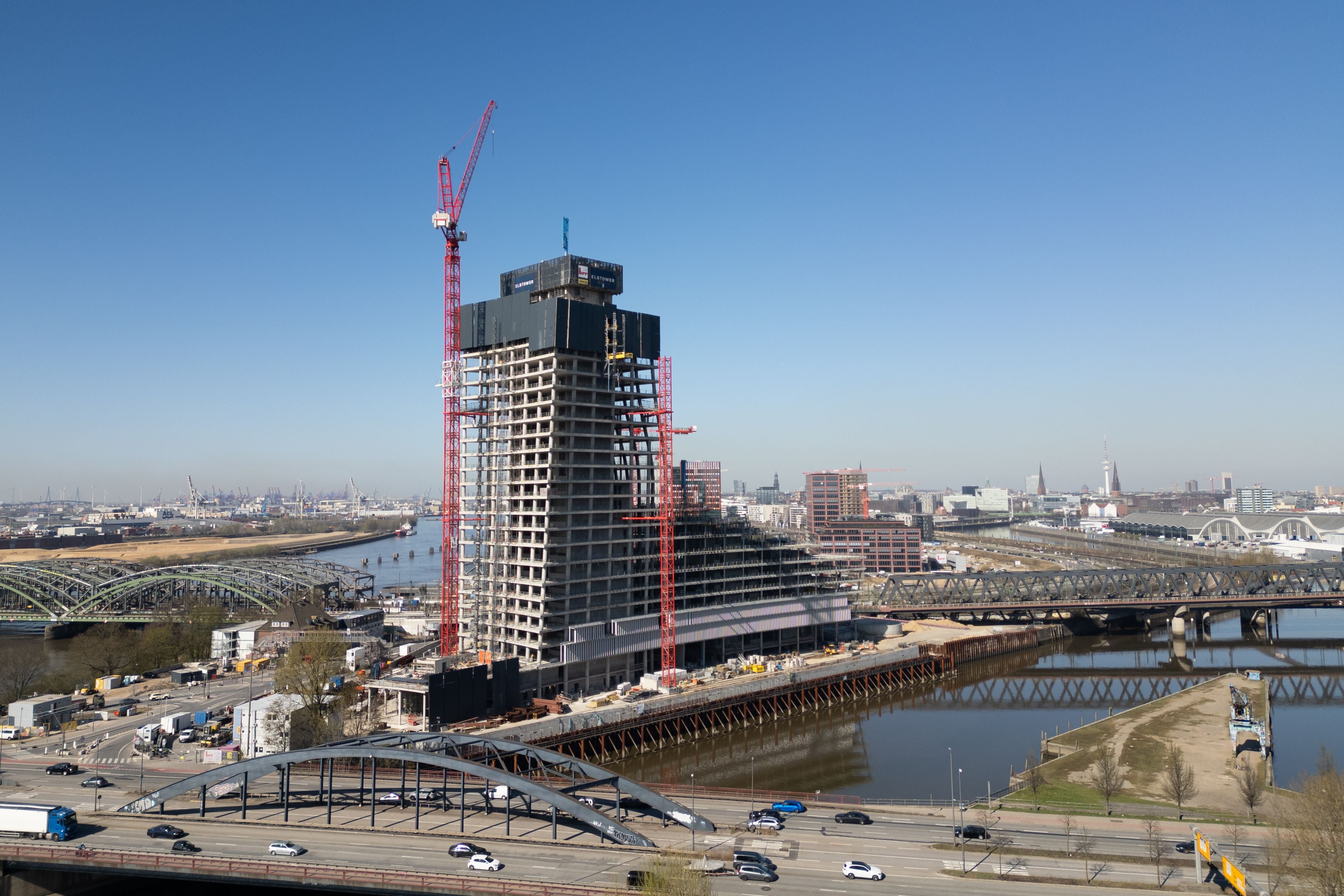 Luftaufnahme des unvollendeten Elbtower mit Baukränen am Hafenrand in Hamburg bei klarem Himmel.