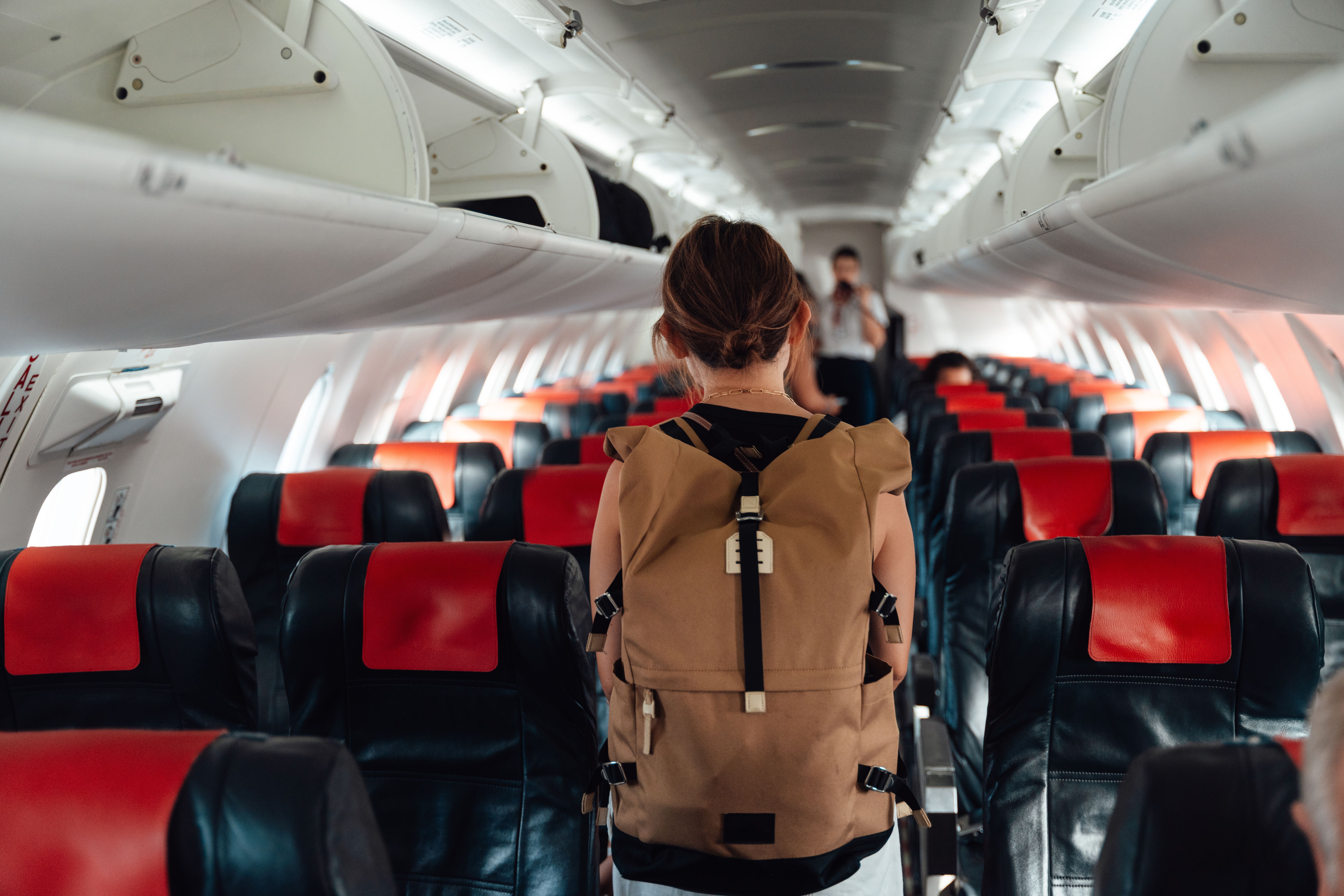 Junge Frau mit Rucksack geht im Flugzeuggang auf der Suche nach ihrem Sitzplatz.