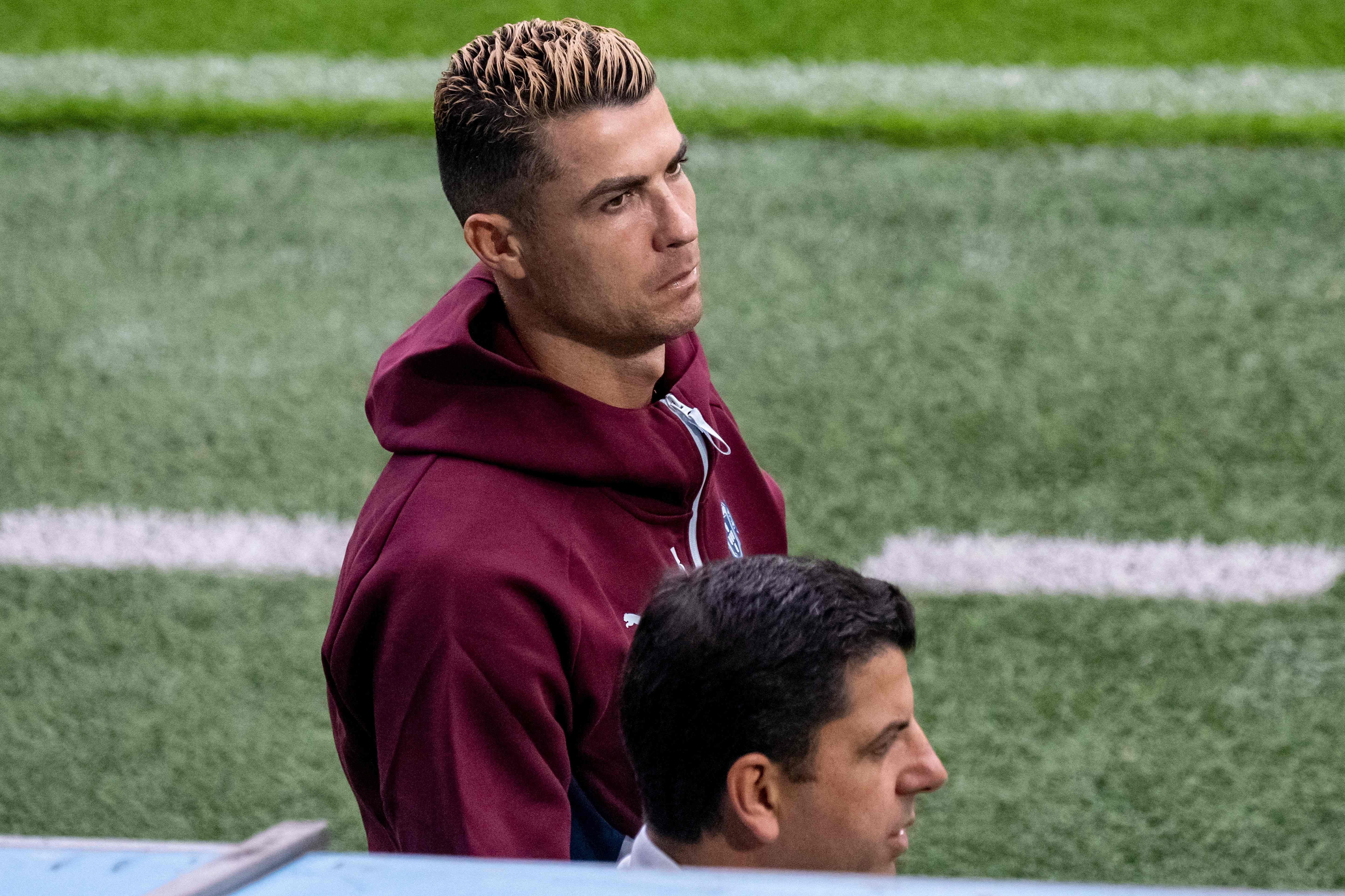 Ein Fußballspieler im bordeauxroten Trainingsanzug steht am Spielfeldrand.