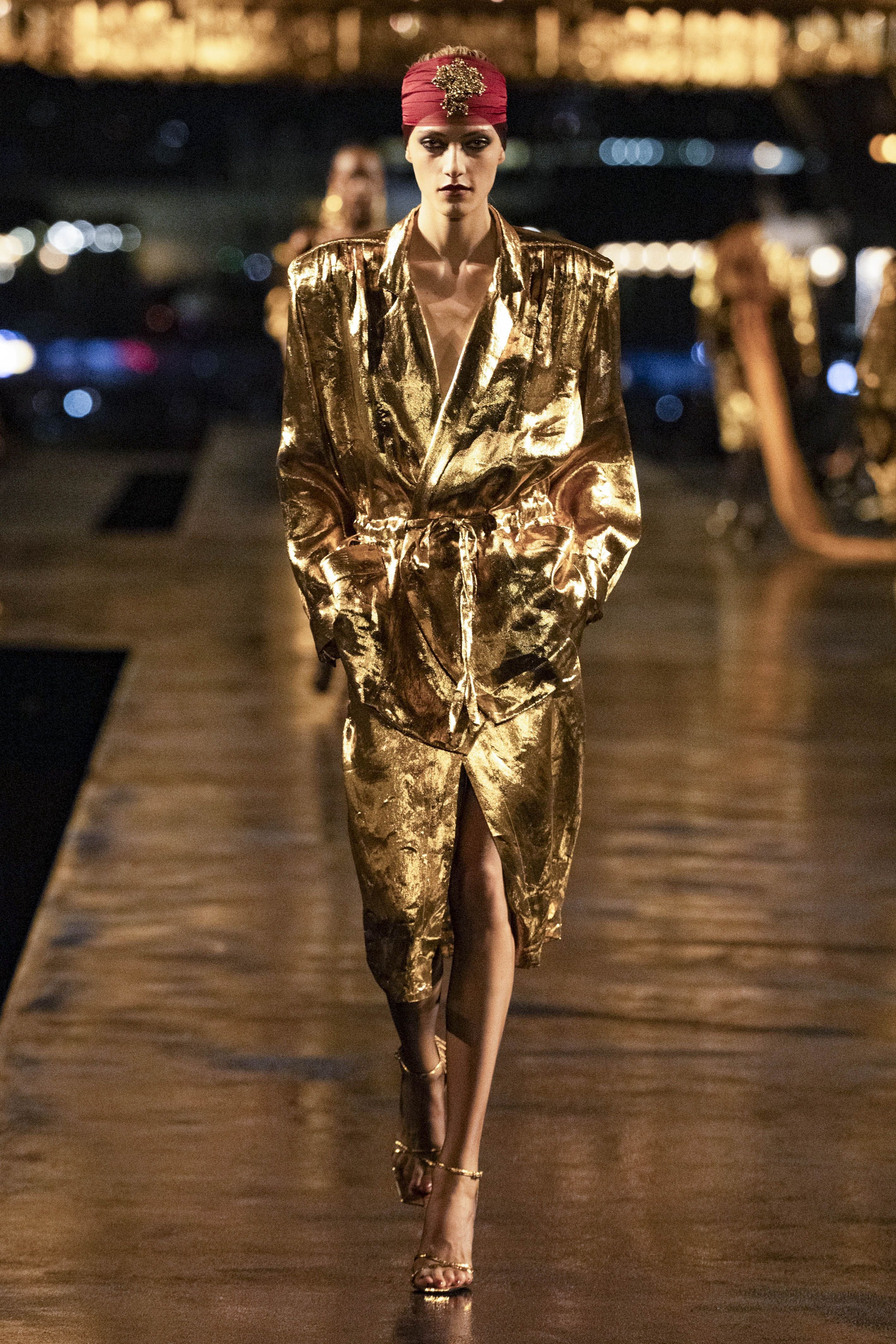 Model in golden Metallic-Mantel mit rotem Turban auf dem Laufsteg bei einer Modenschau.