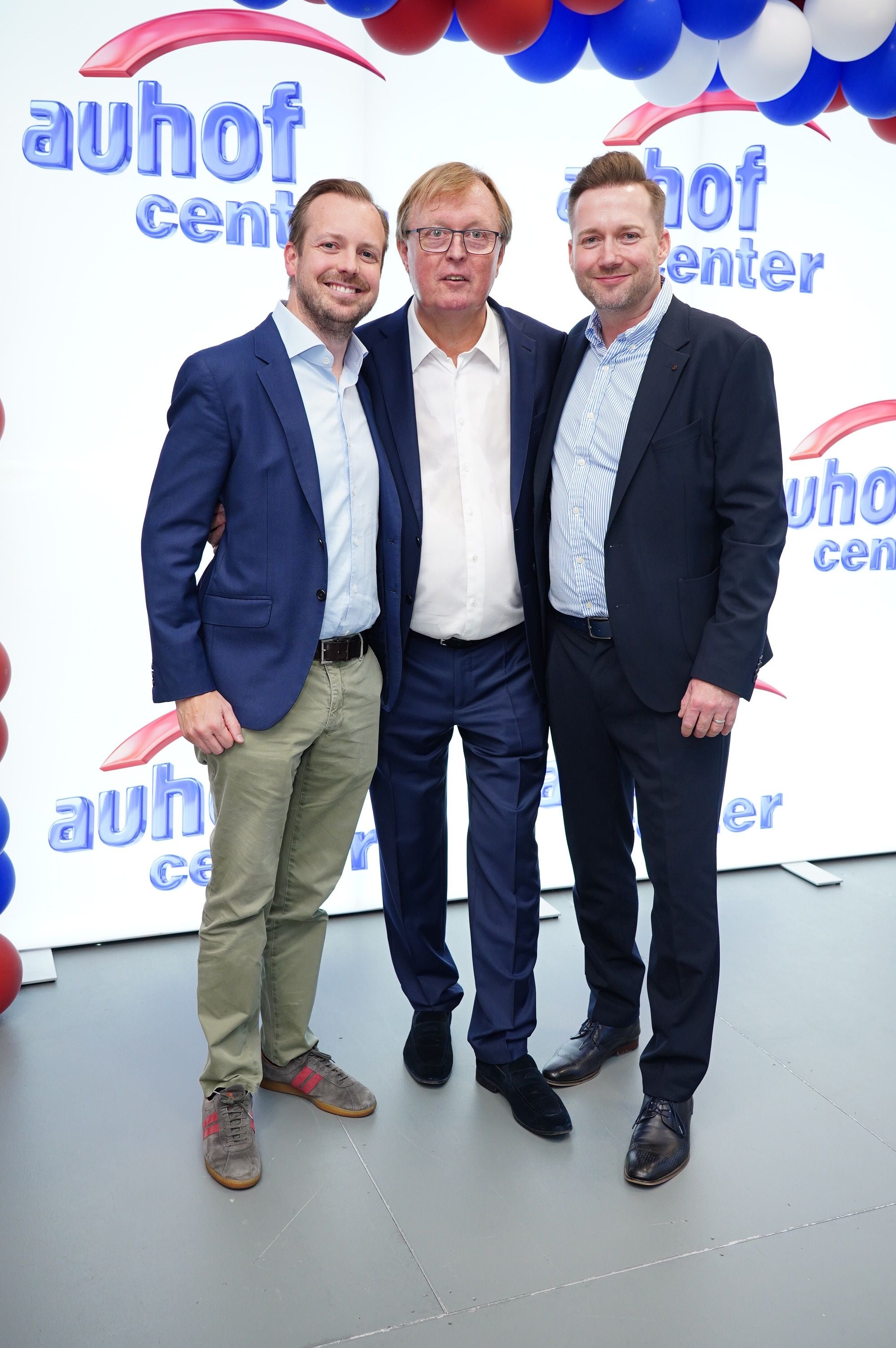 Drei Männer in Anzügen posieren lächelnd vor einem "Auhofcenter"-Hintergrund.