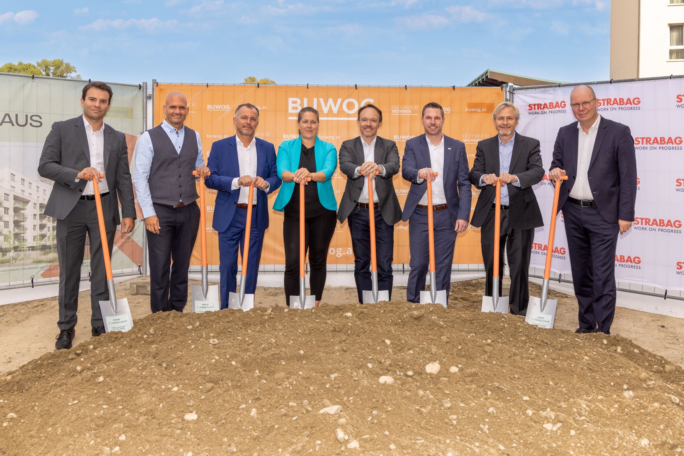 Acht Menschen stehen mit Spaten vor einem Erdhaufen auf einer Baustelle beim Spatenstich.