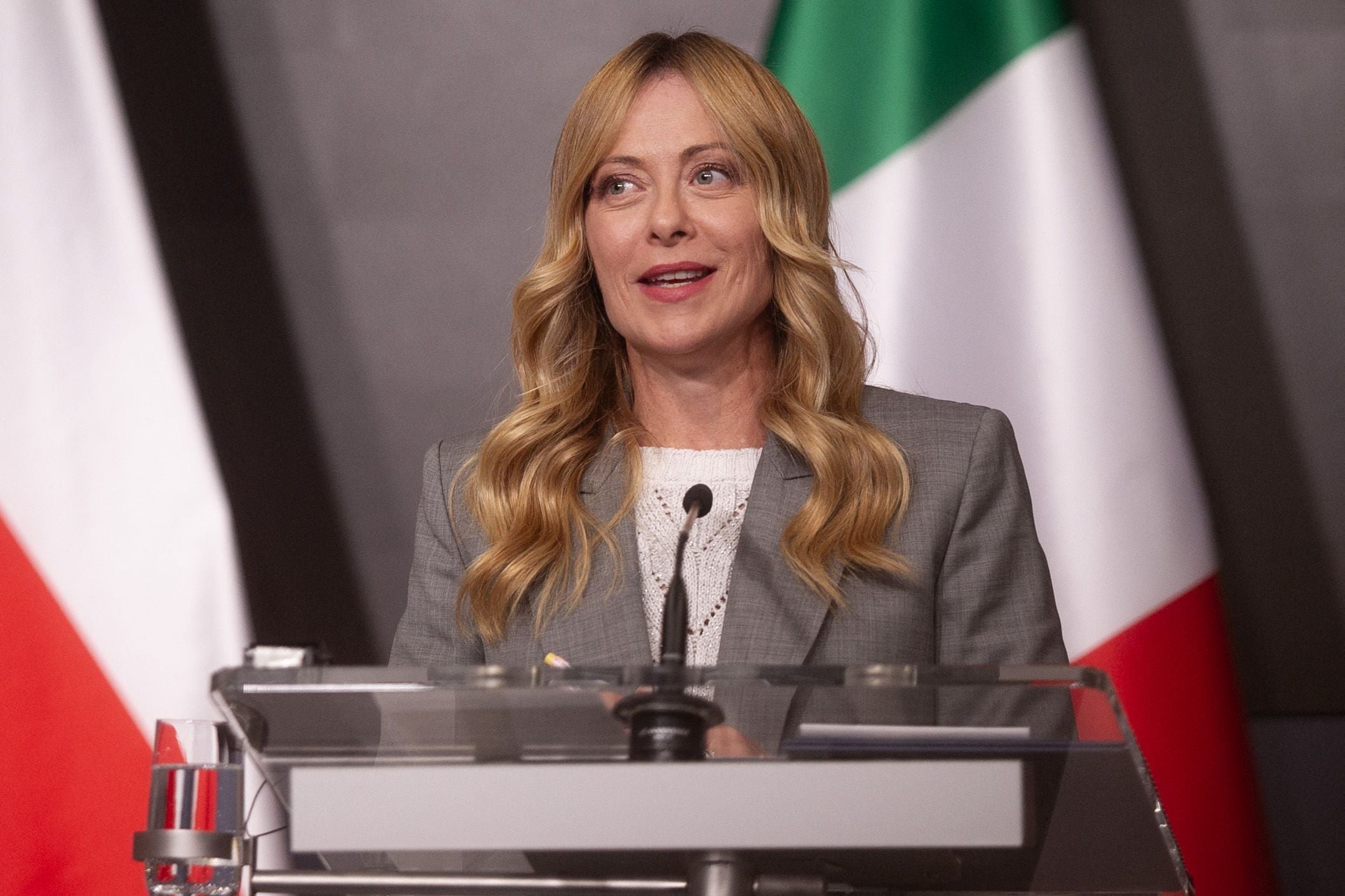 Eine Frau hält eine Rede an einem Rednerpult vor italienischer Flagge im Hintergrund.