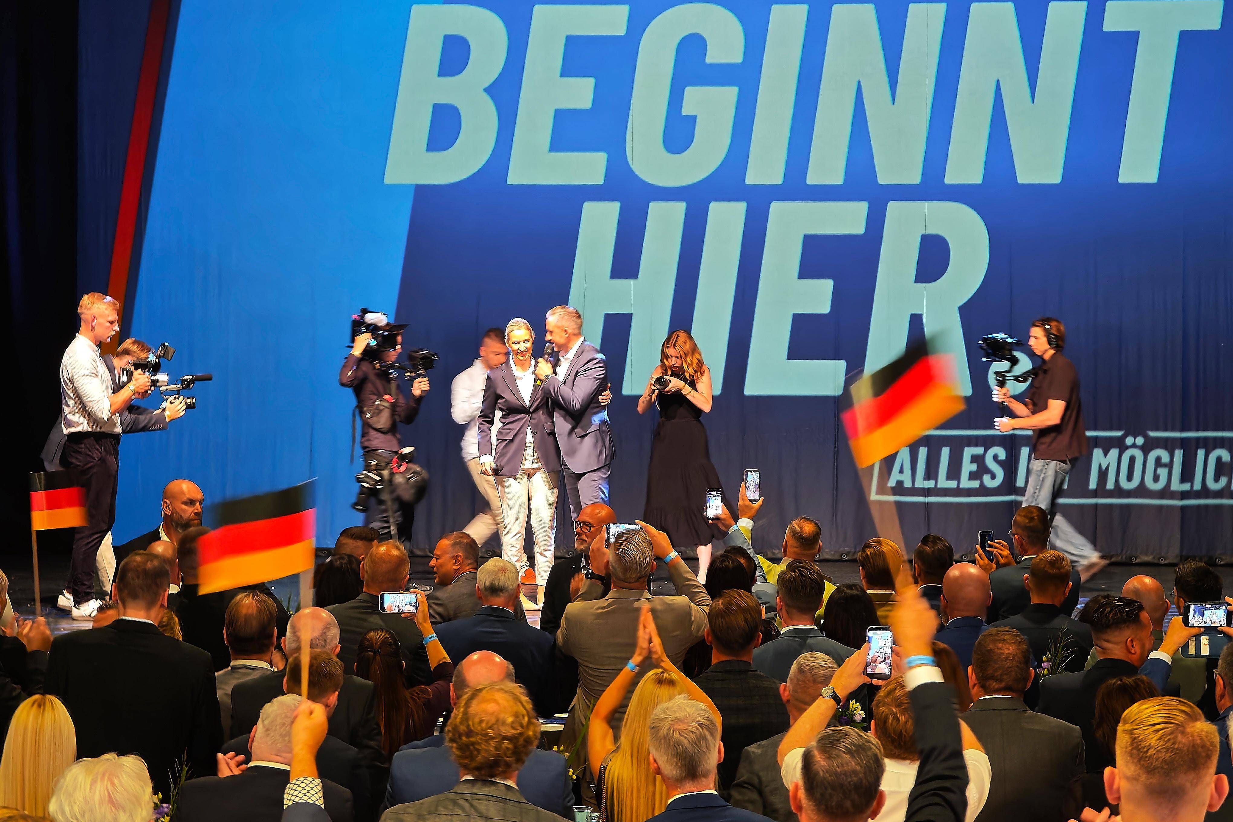AfD-Wahlparty 2026 in Magdeburg mit Menschen auf der Bühne und feierndem Publikum mit Deutschlandfahnen.
