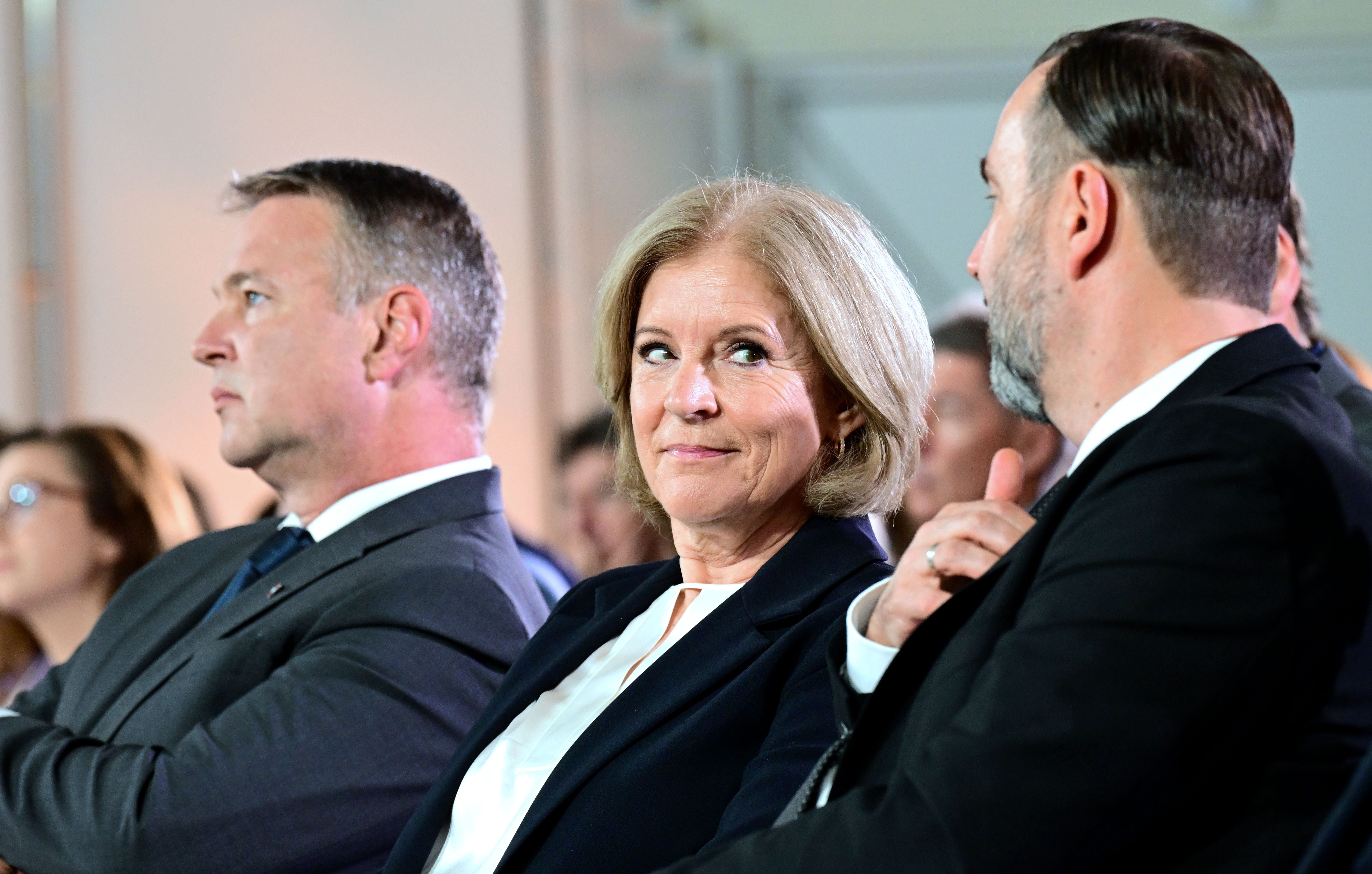Drei Personen im Anzug sitzen nebeneinander bei einer Veranstaltung in Wien.