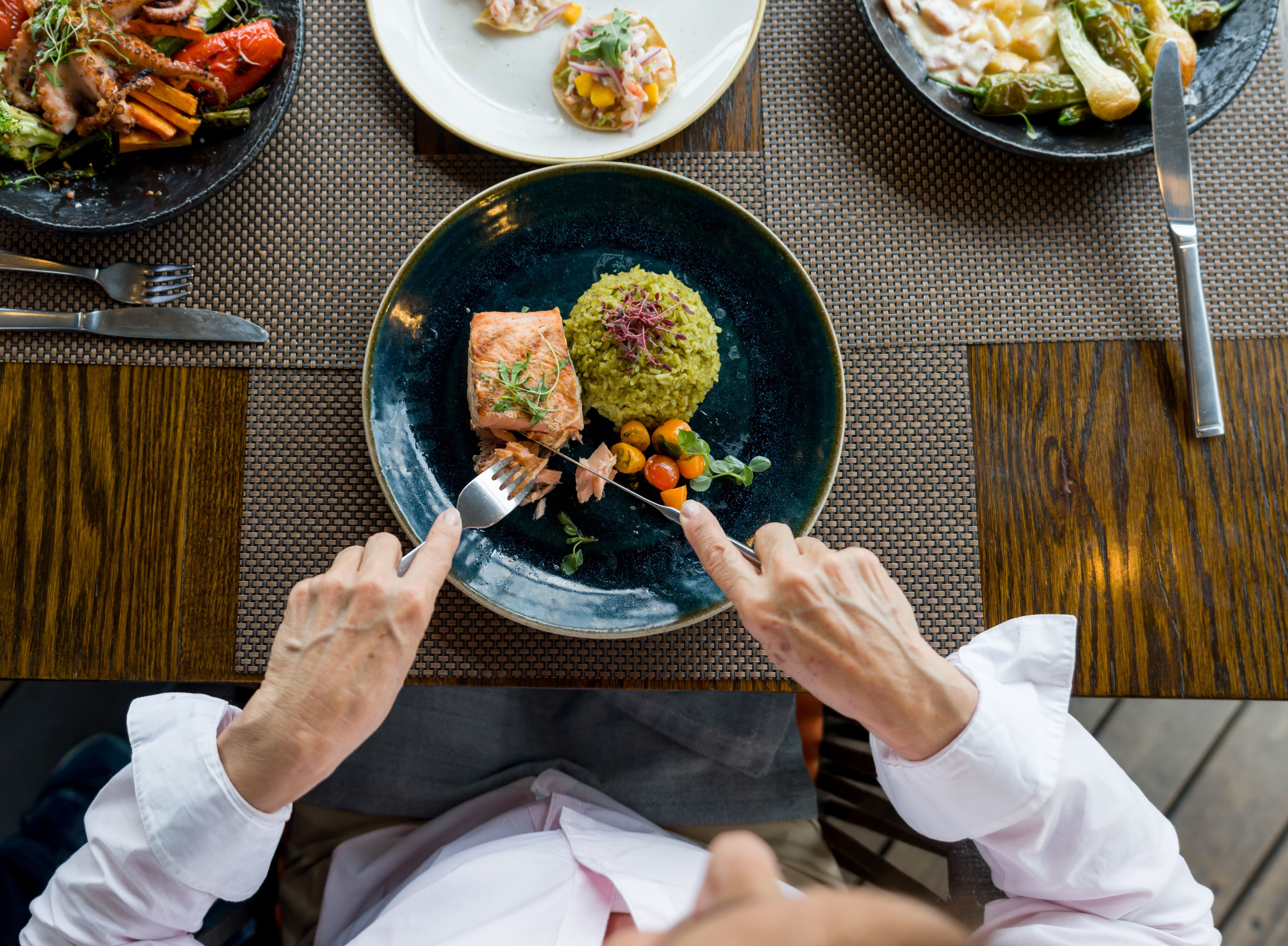 Frau isst Lachs mit Reis und Gemüse in einem Restaurant, Ansicht von oben.