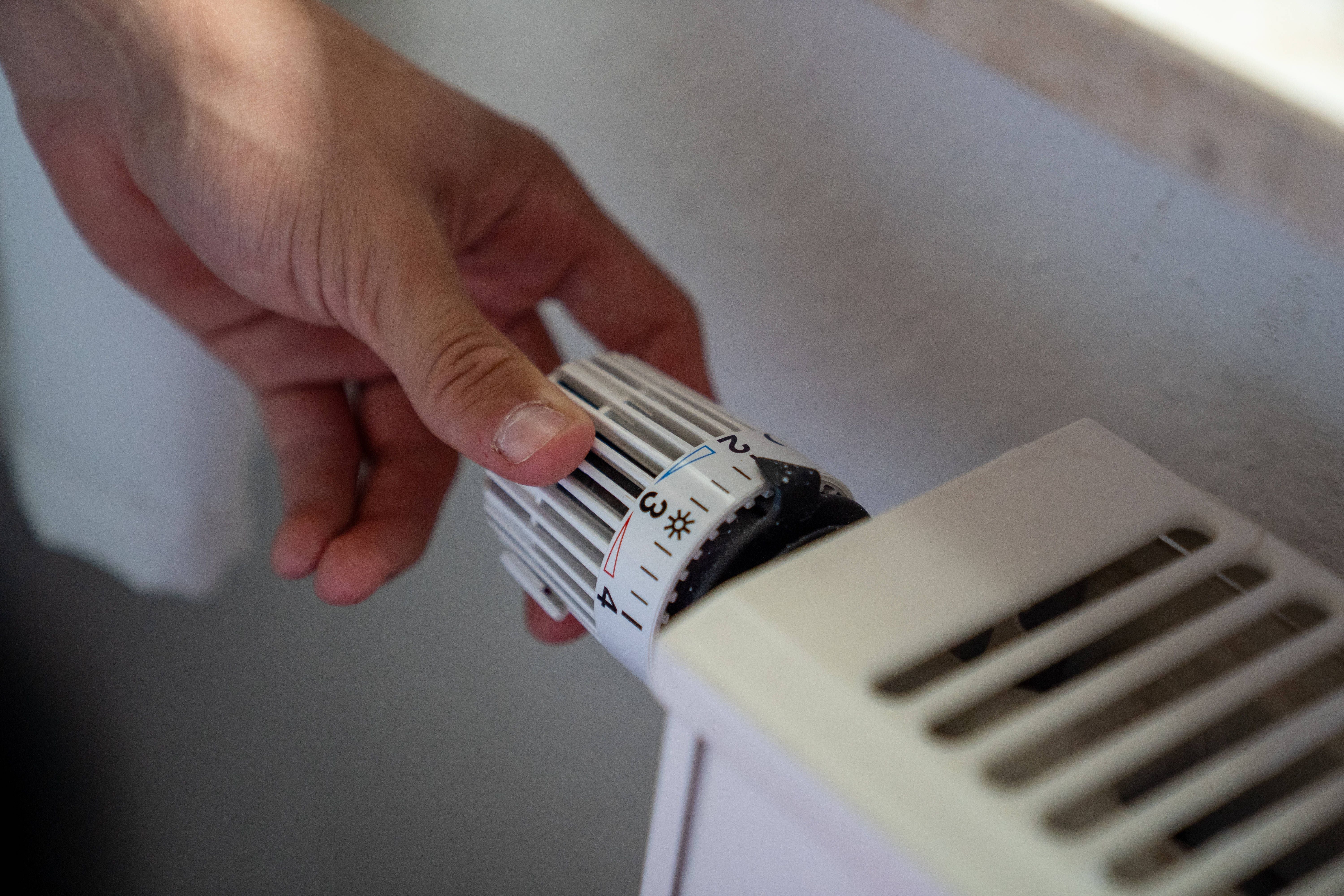 Eine Hand dreht den Thermostatregler an einem weißen Heizkörper.