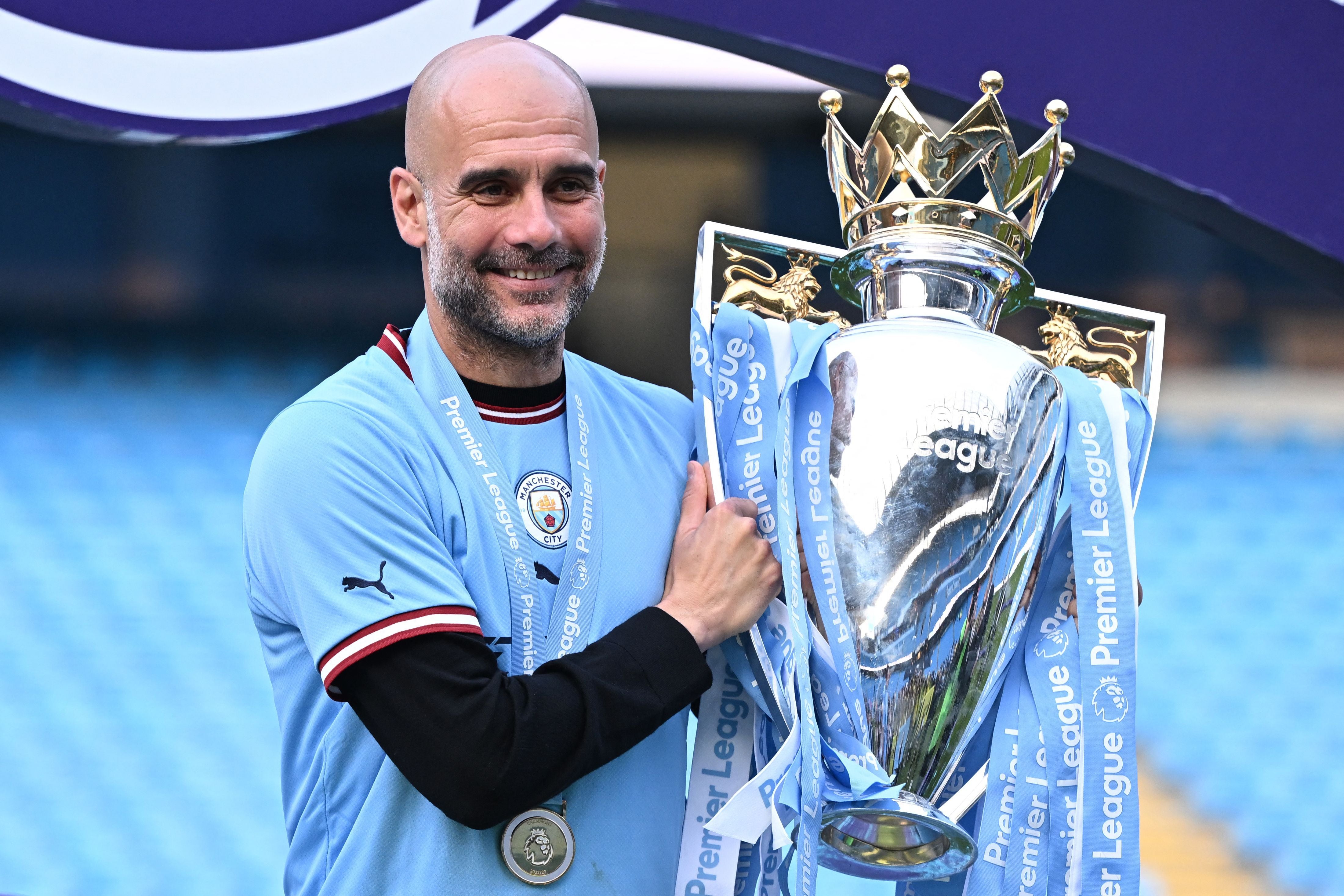 Ein Mann im Manchester City-Trikot hält die Premier League-Trophäe und lächelt.