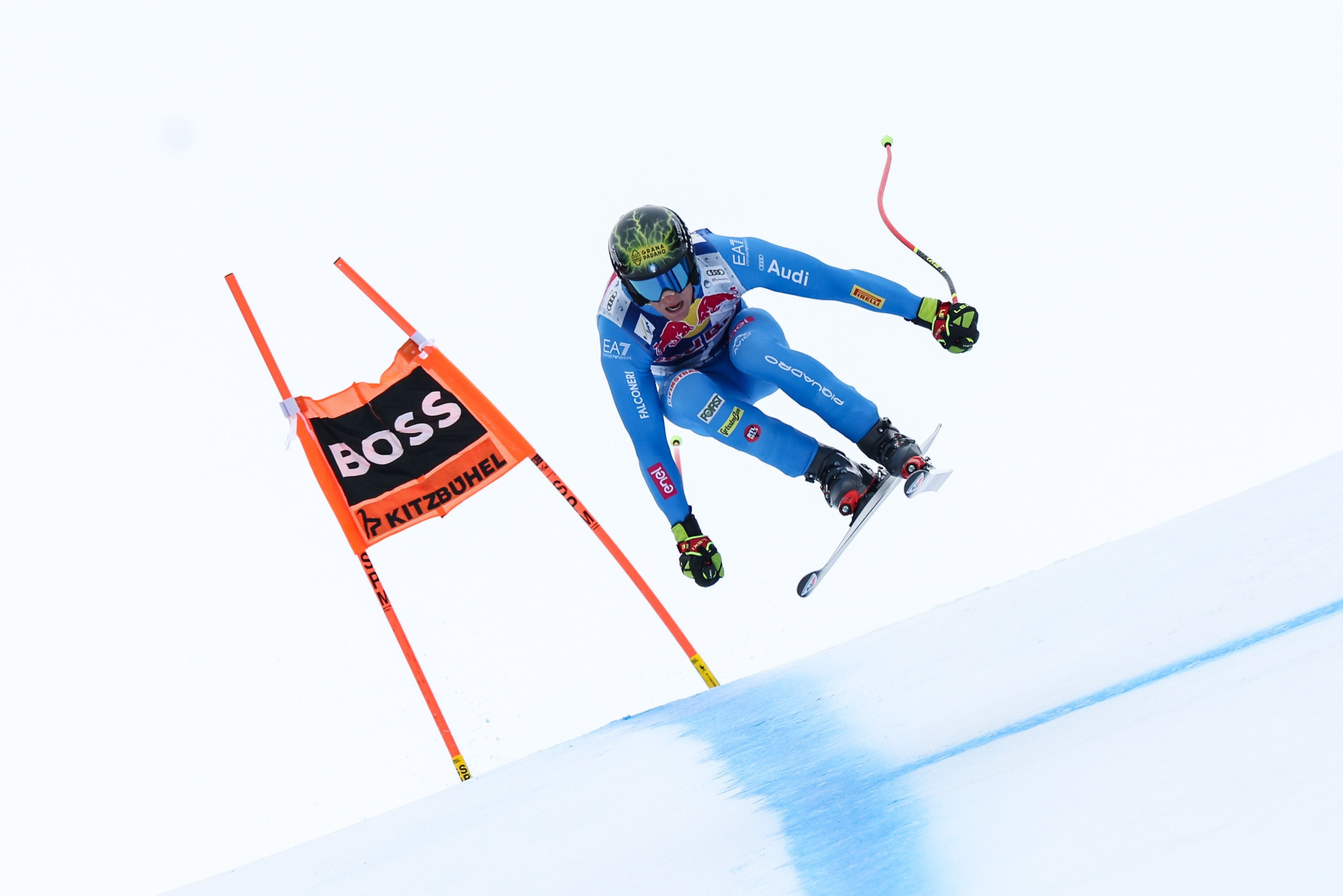 Ein Skirennläufer springt bei einem Abfahrtsrennen in Kitzbühel neben einer roten Torflagge.