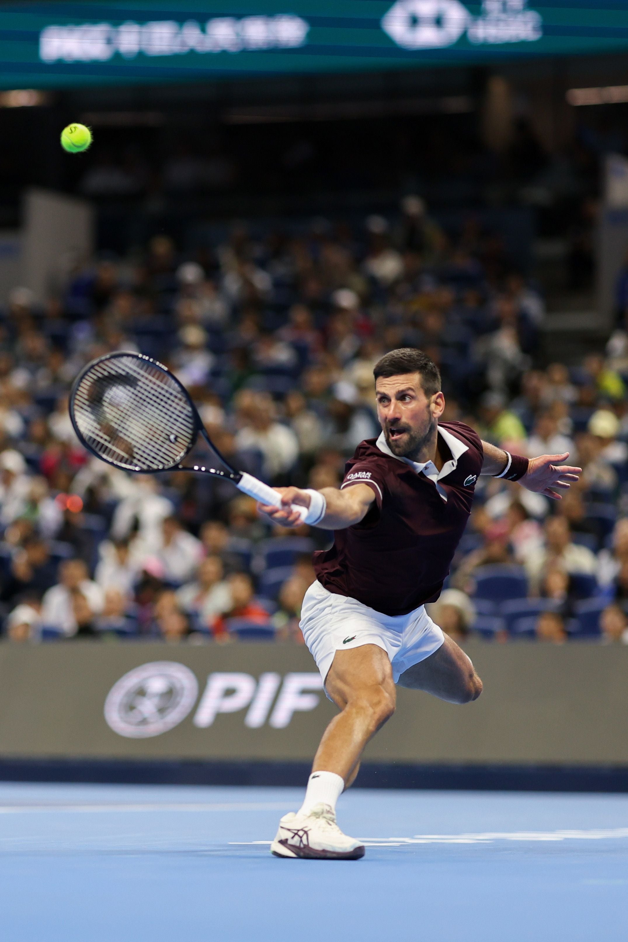 Ein Tennisspieler schlägt auf einem Hartplatz einen Ball mit einer Vorhand zurück.
