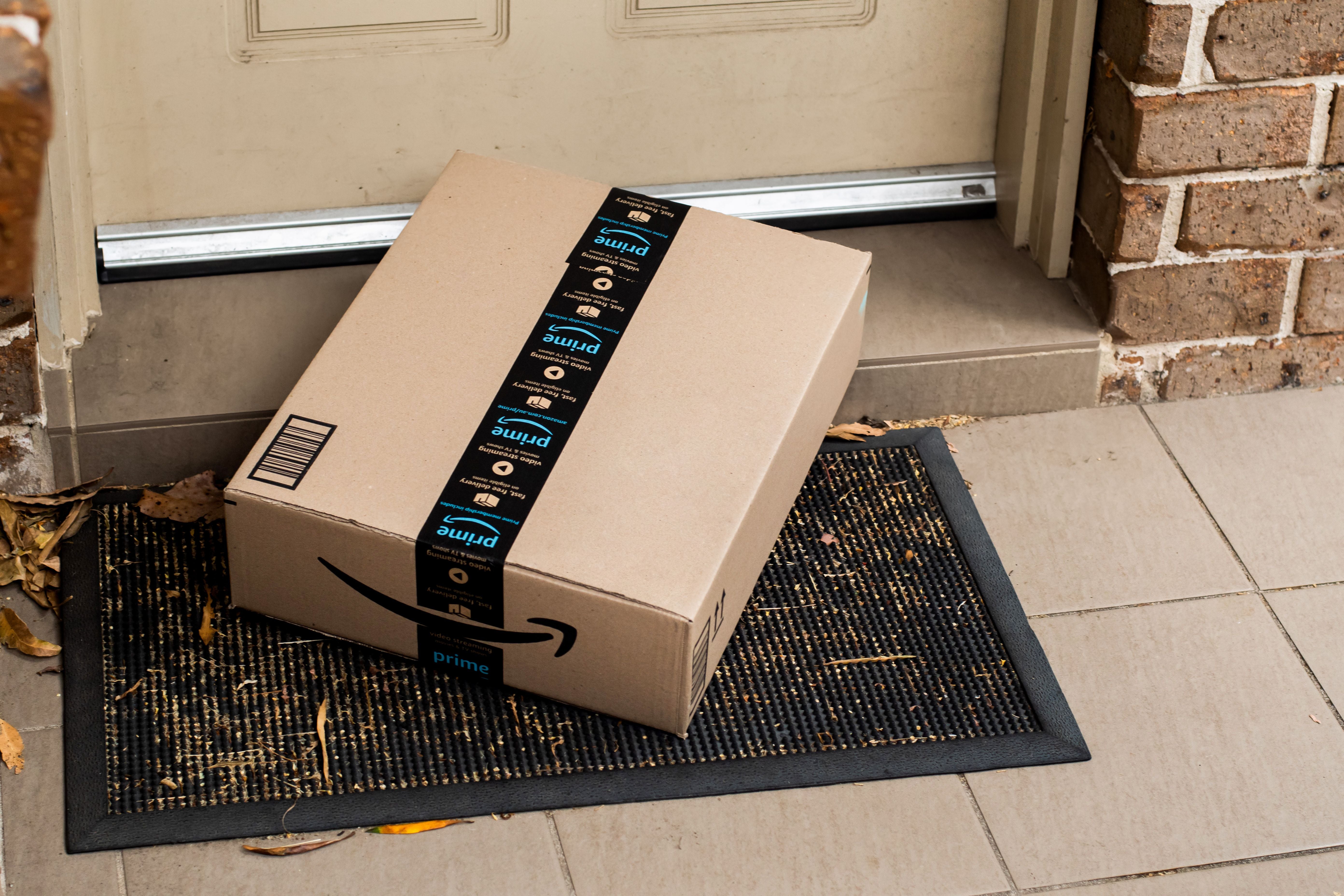 Ein Amazon Prime Paket liegt auf einer Fußmatte vor einer Haustür.