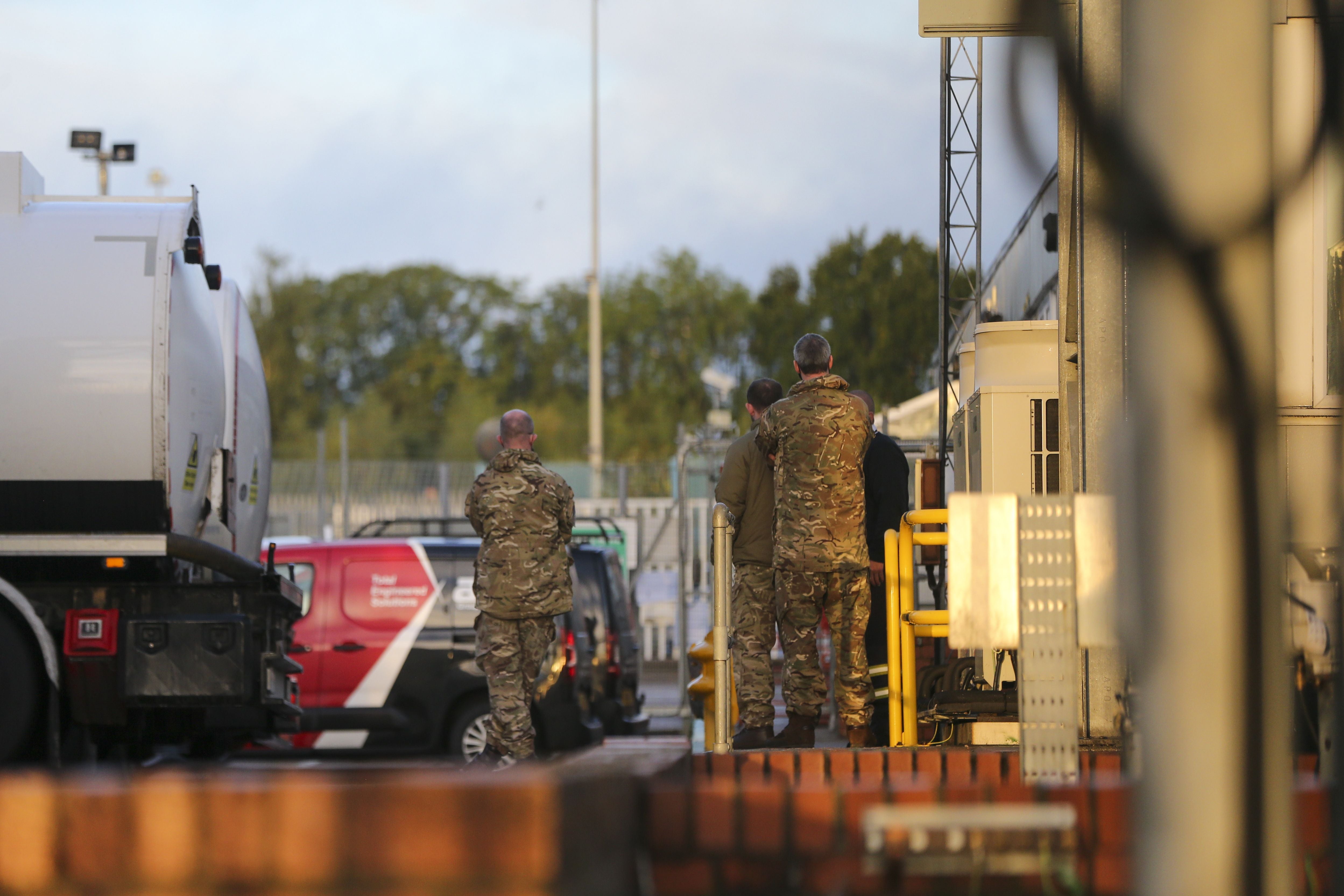 Mehrere Soldaten in Tarnuniform stehen an einem Öldepot neben Lastwagen und technischen Anlagen.