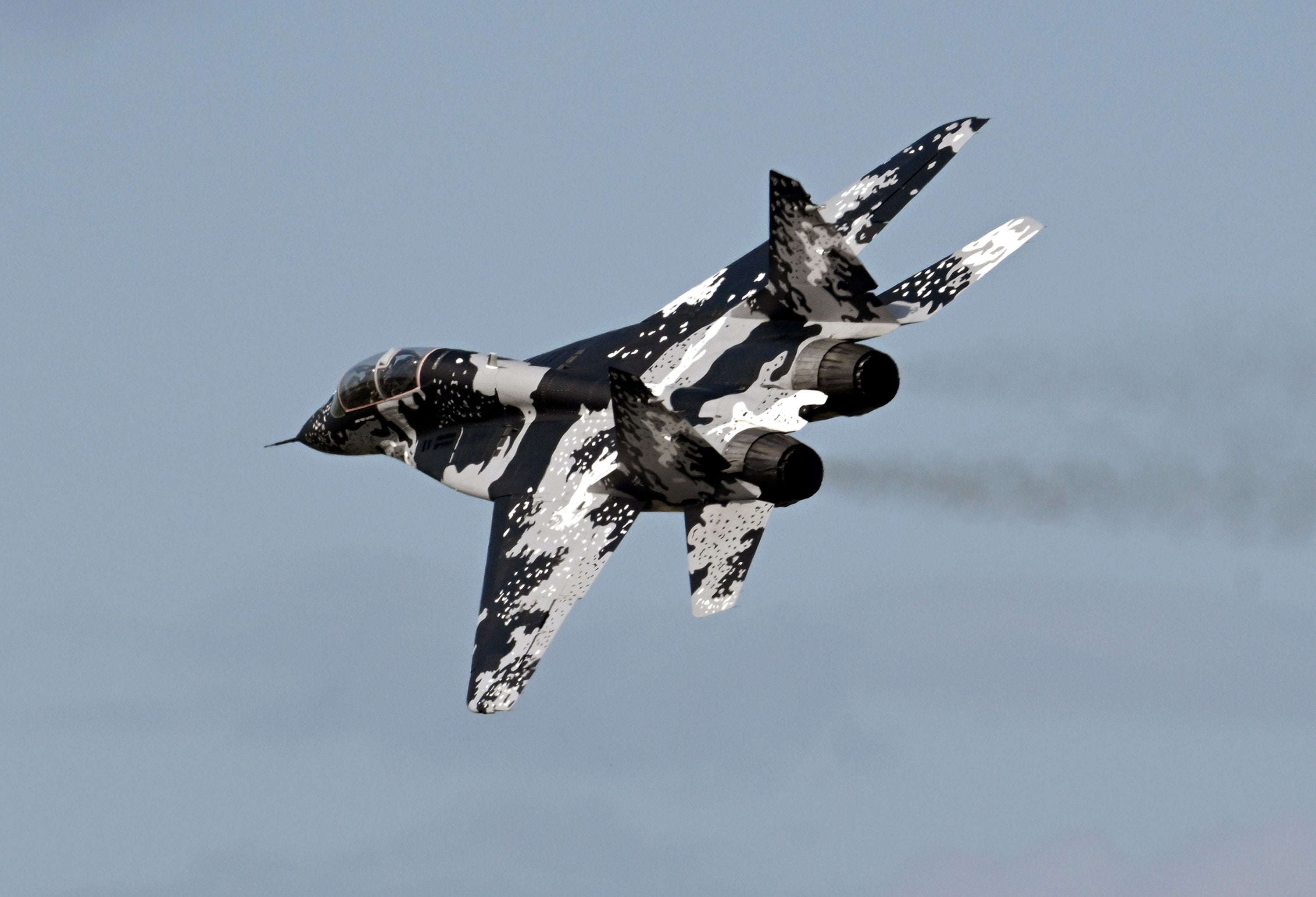 Ein MiG-29-Kampfjet mit Tarnmuster fliegt am Himmel, von hinten fotografiert.