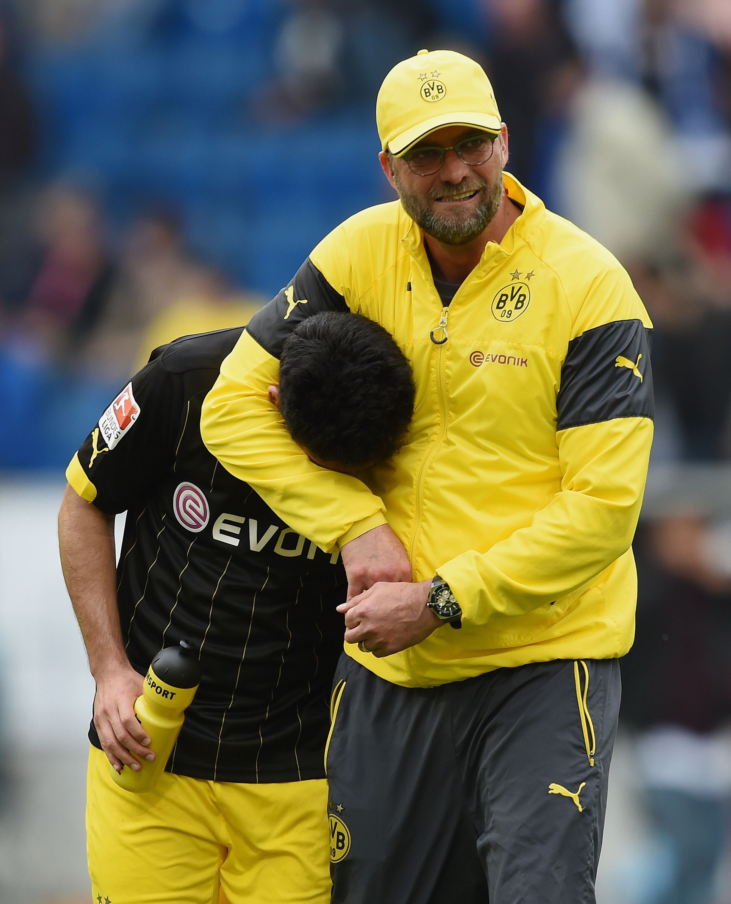 Jürgen Klopp umarmt lachend einen Dortmunder Spieler auf dem Fußballfeld.