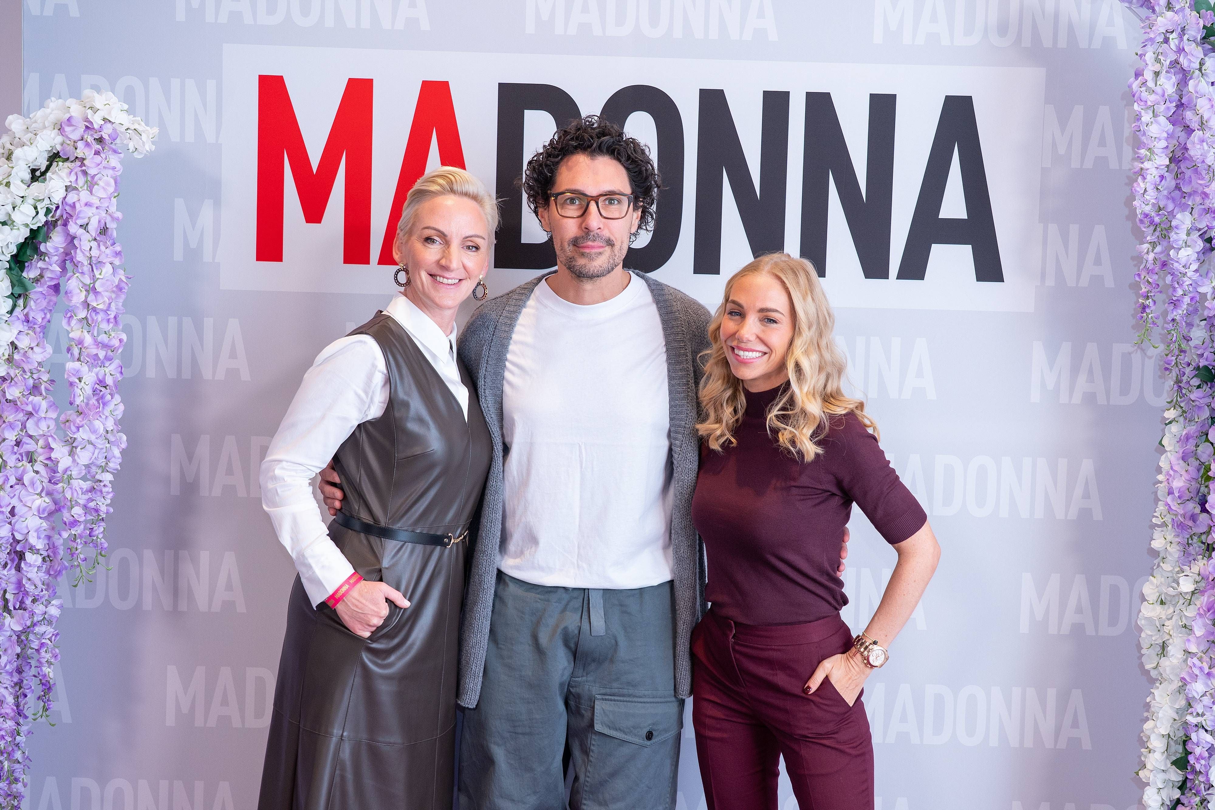 Drei Personen posieren vor einem „MADONNA“-Schriftzug bei einer Veranstaltung in Wien.
