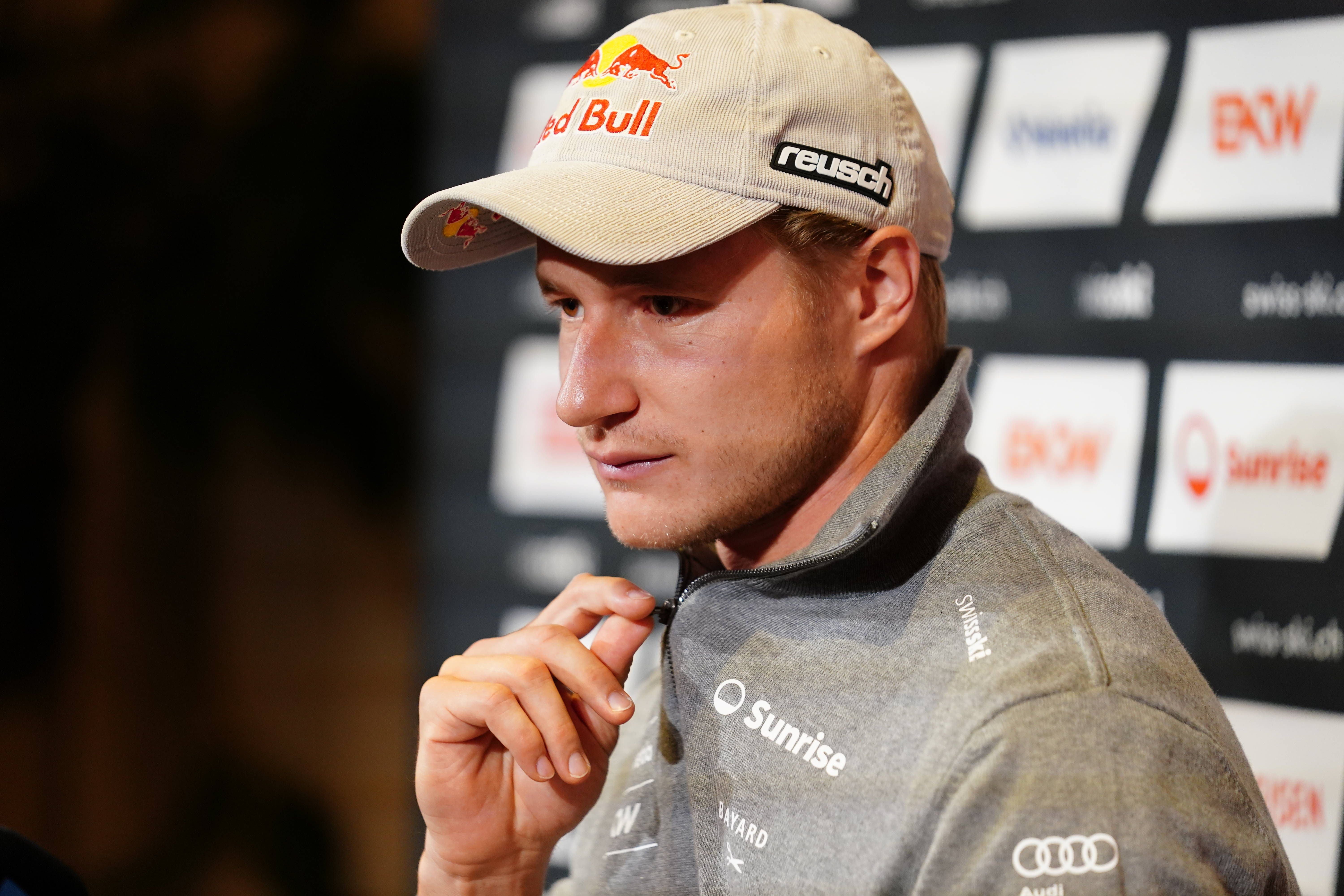 Ein Mann mit Red-Bull-Cap und grauer Jacke spricht bei einem Medientermin vor Sponsorenwänden.