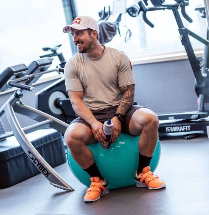 Ein Mann sitzt auf einem Gymnastikball im Fitnessstudio und hält eine Trinkflasche.