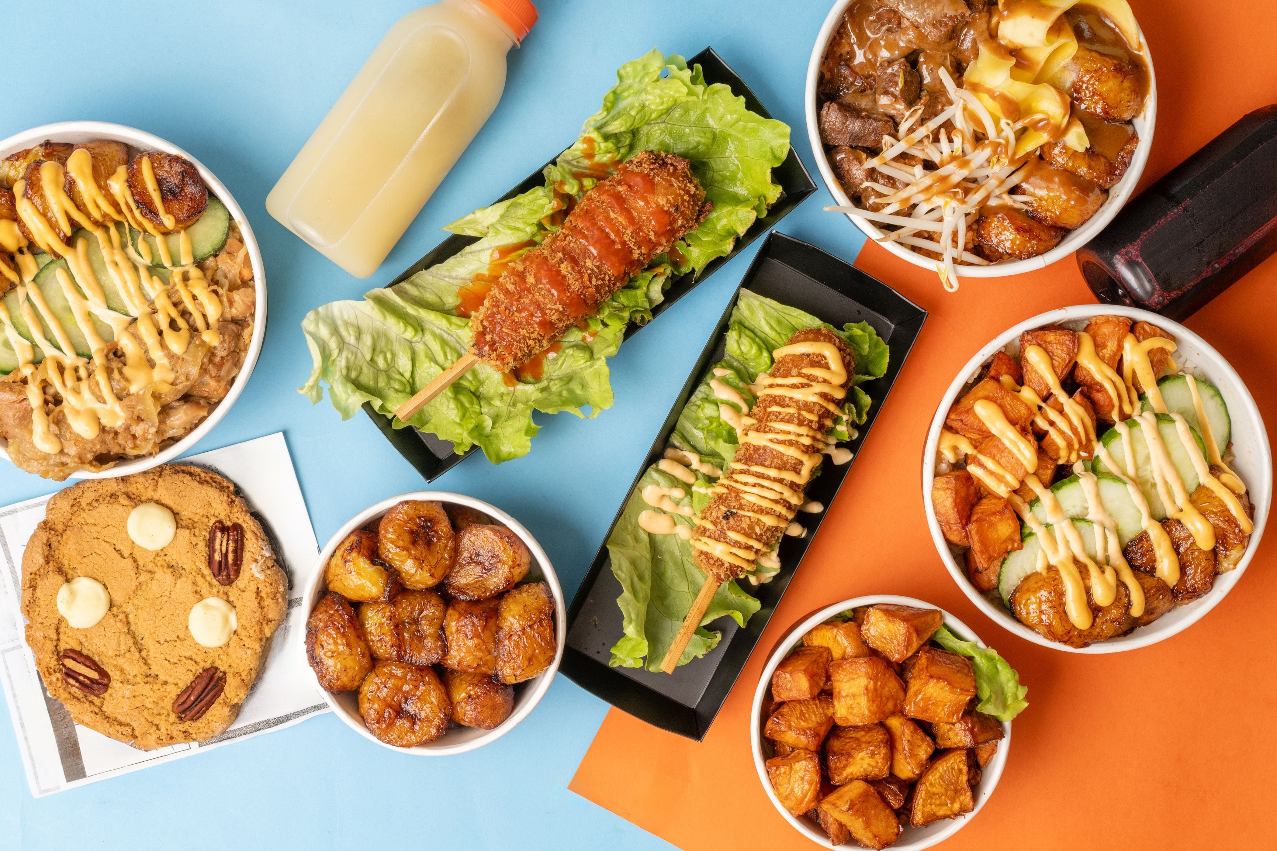 Verschiedene Poke Bowls, frittierte Snacks, ein Keks und zwei Getränke auf buntem Untergrund.