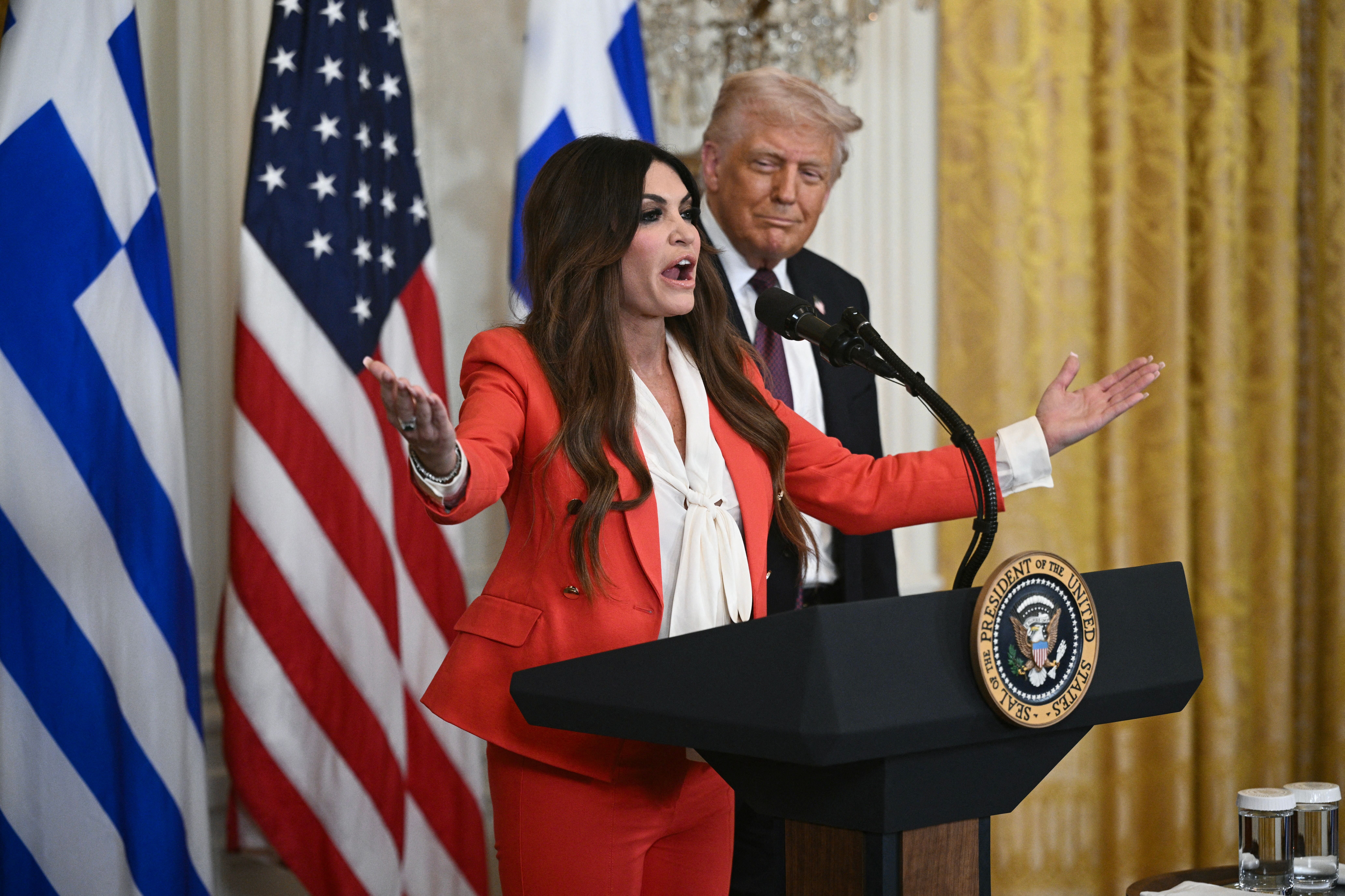 Eine Frau spricht am Rednerpult im Weißen Haus, ein Mann steht dahinter, US- und griechische Flaggen im Hintergrund.