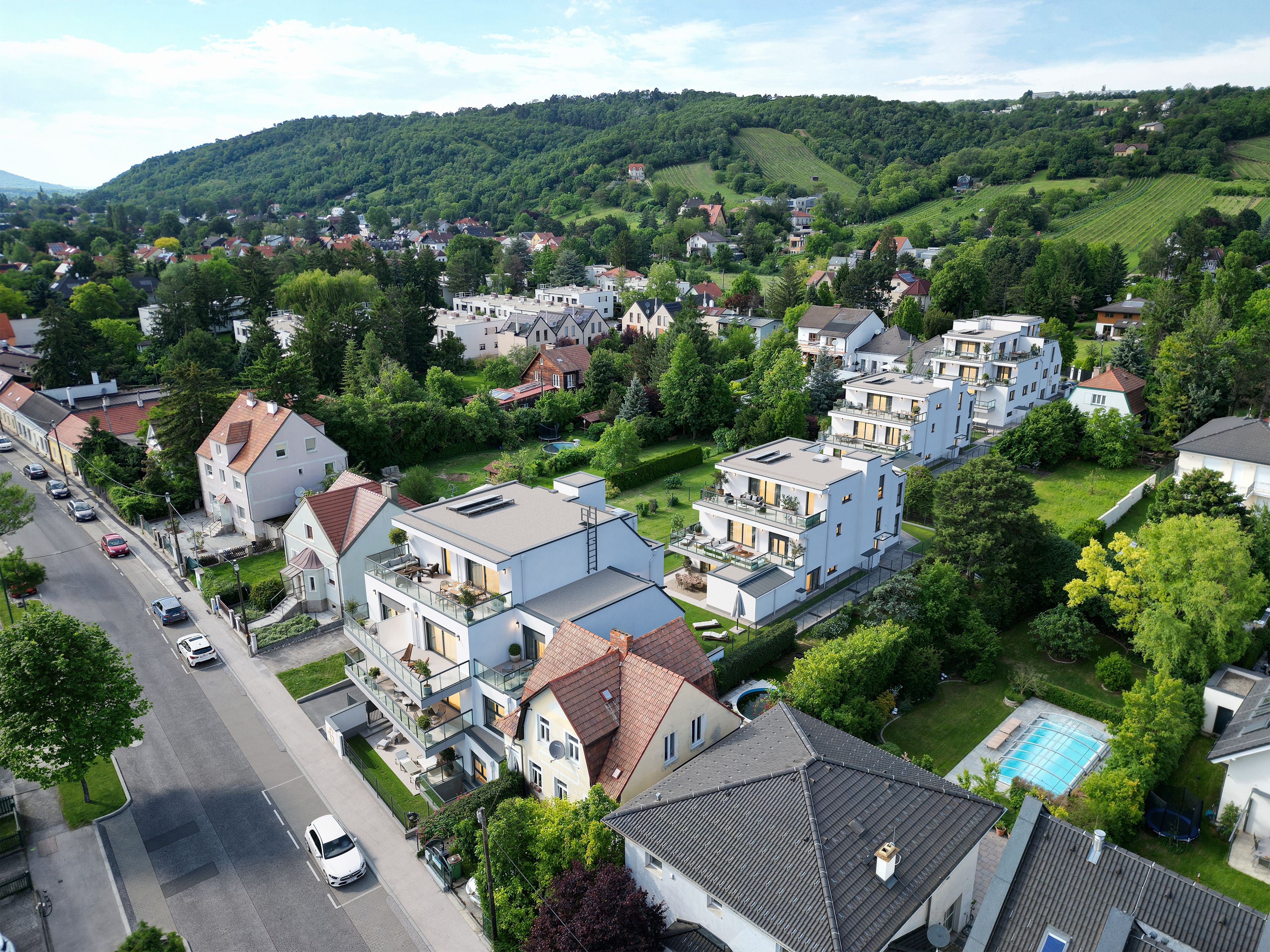 Luftaufnahme eines Wohngebiets mit modernen Häusern, Straßen und viel Grün in hügeliger Umgebung.