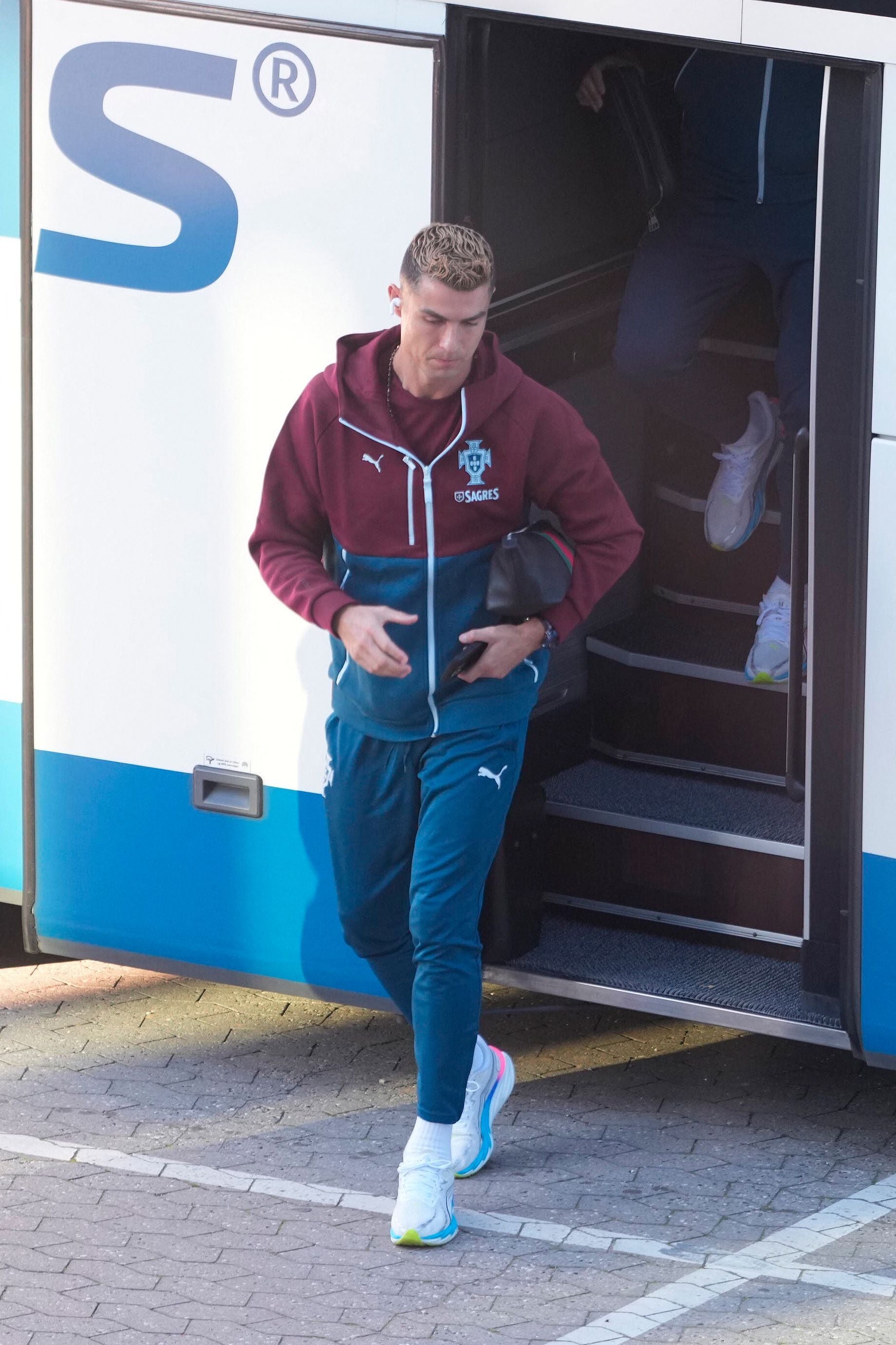 Ein Fußballspieler im Trainingsanzug steigt aus einem Bus und hält eine kleine Tasche in der Hand.