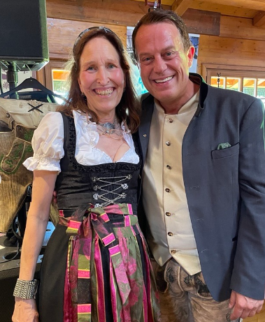 Ein lächelndes Paar in traditioneller bayerischer Tracht posiert in einem Holzraum.