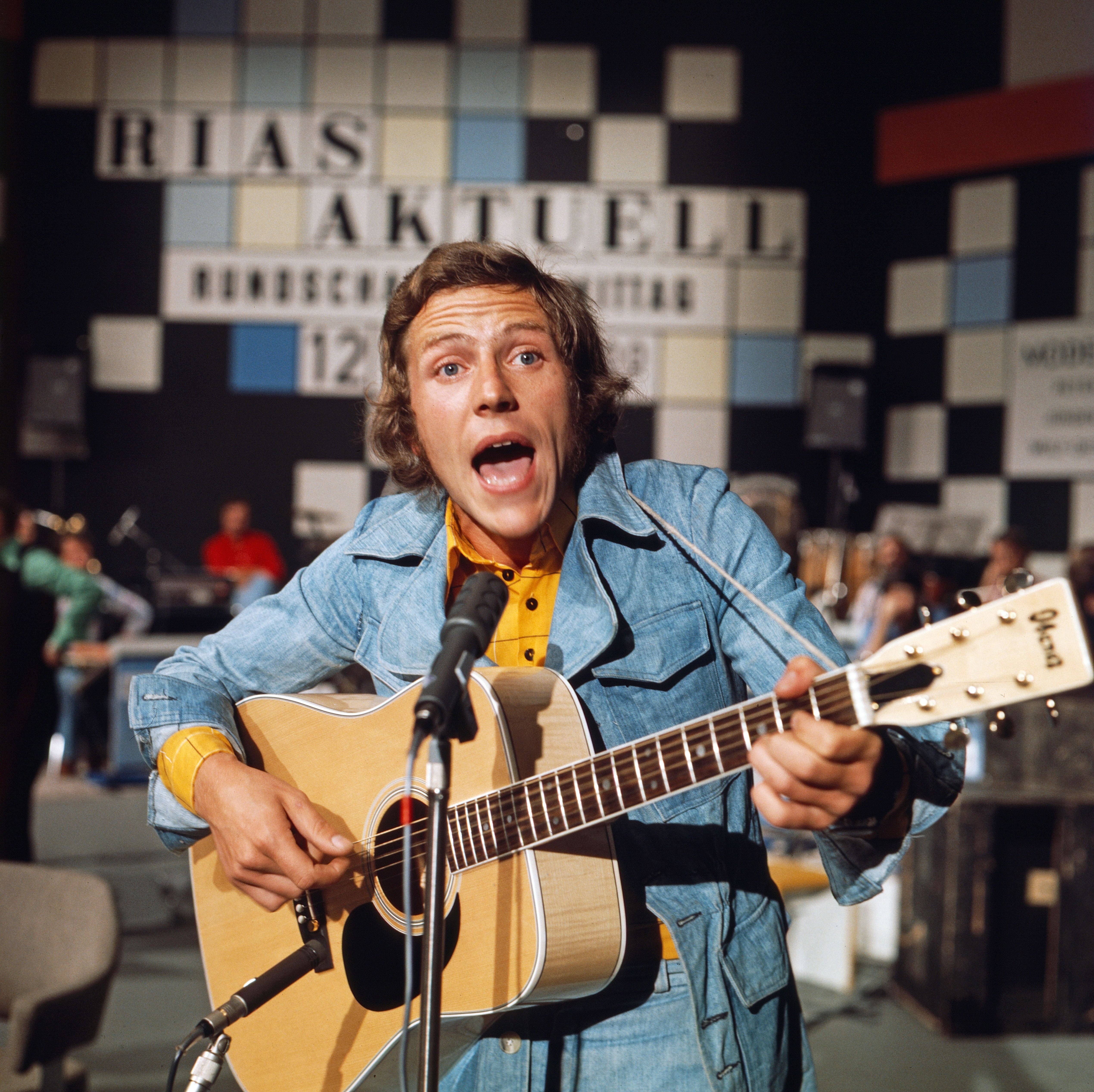 Ein Sänger mit Gitarre tritt 1975 in einer Fernsehshow vor einem Mikrofon auf.
