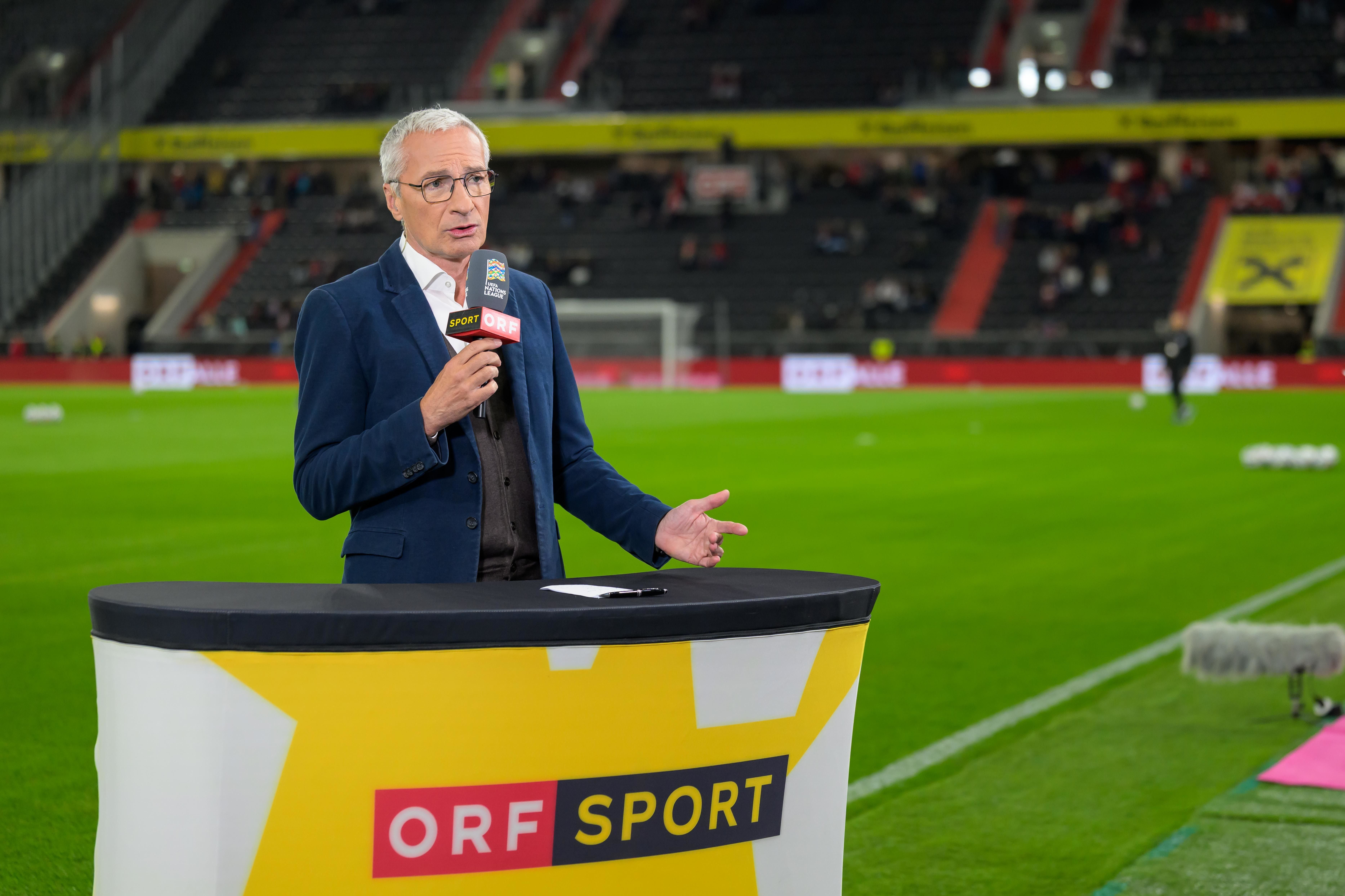 Ein Sportmoderator spricht auf dem Fußballfeld für ORF Sport in einem leeren Stadion.