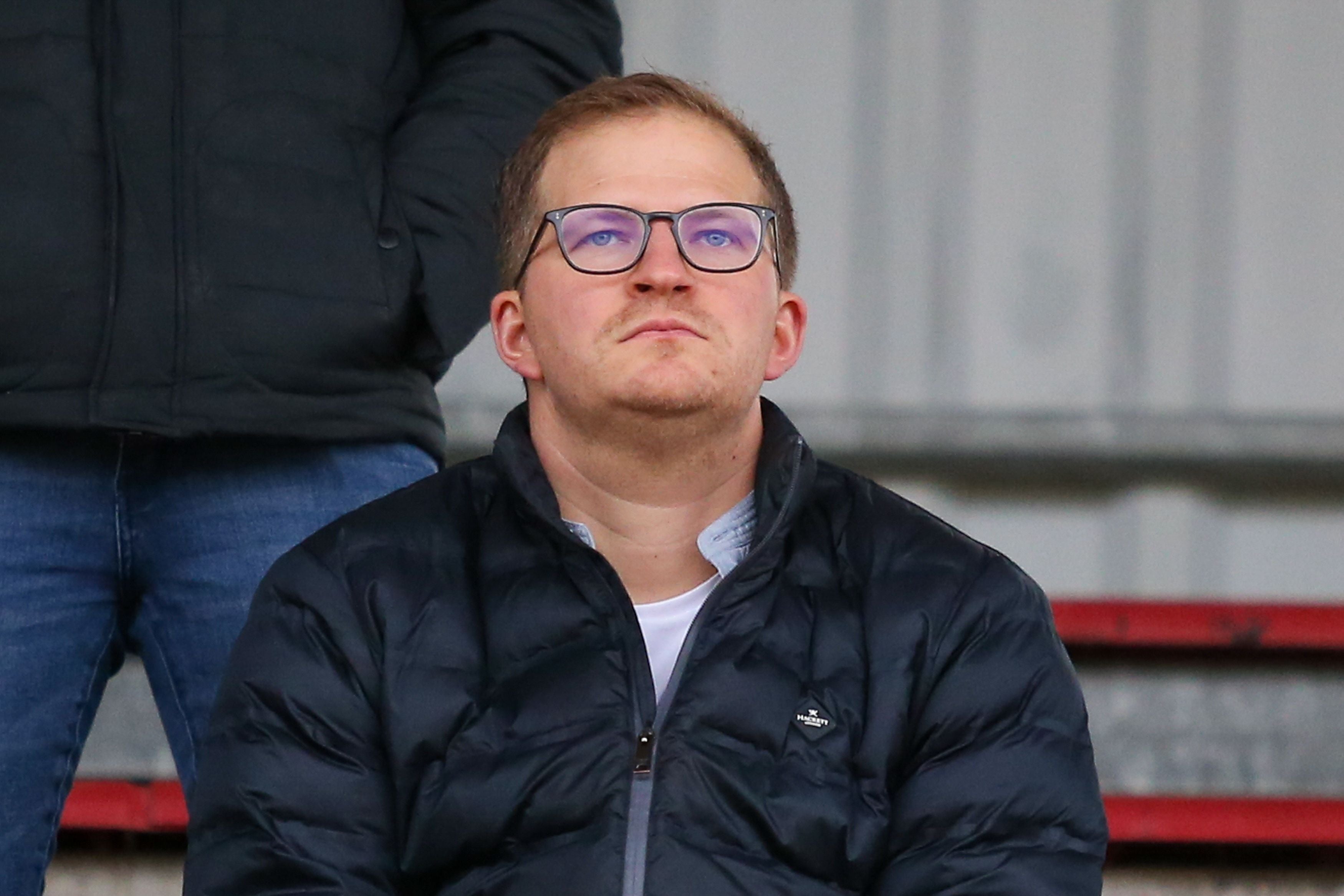 Wolfgang Fiala blickt mit Brille und dunkler Jacke auf der Tribüne nach oben.