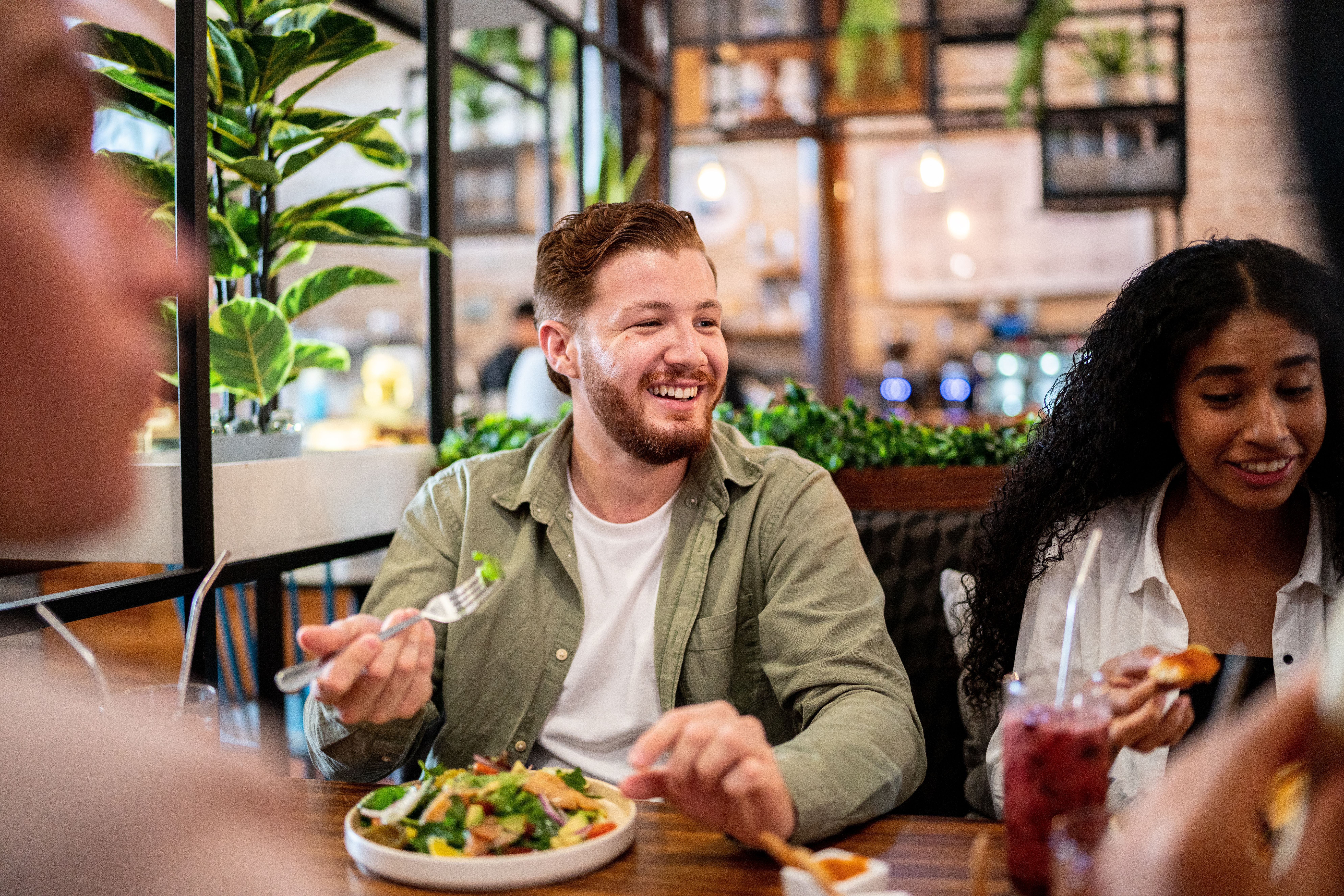 Junger Mann isst mit Freunden in einem Restaurant und lacht.