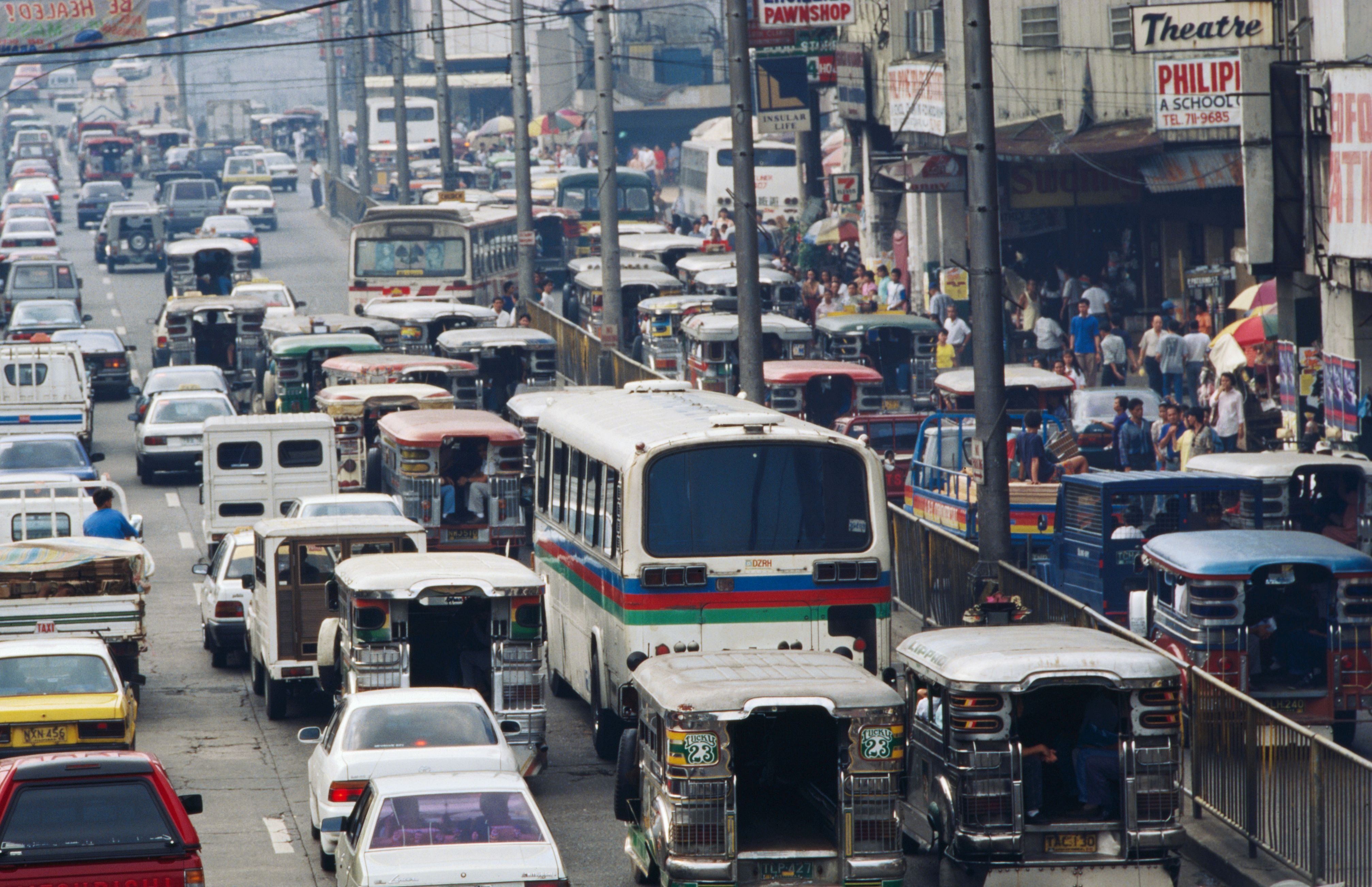 Dichter Straßenverkehr mit Bussen und Jeepneys in Manila, Menschenmengen auf dem Gehweg.