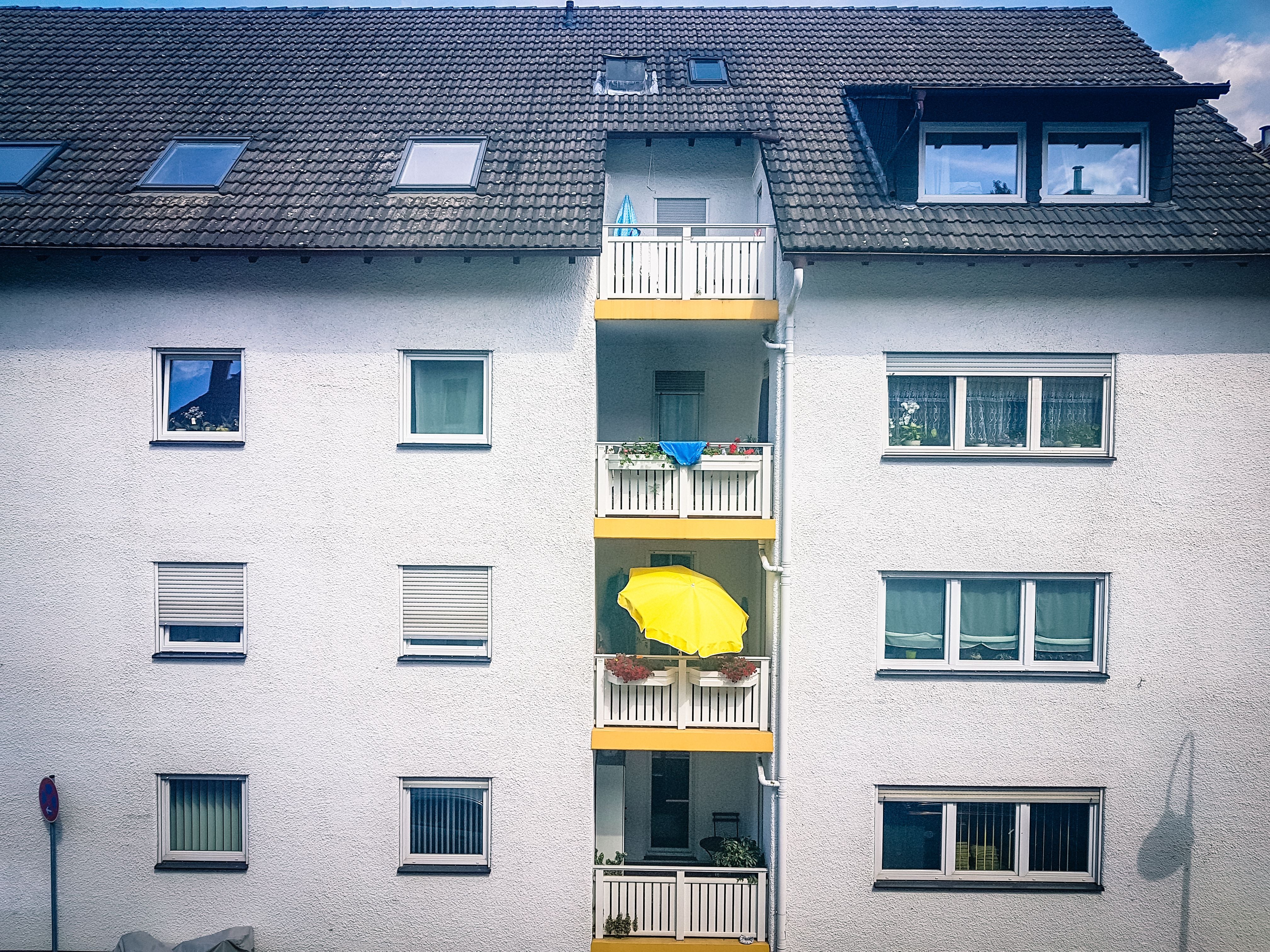 Mehrstöckiges Wohnhaus mit gelbem Sonnenschirm auf einem mittleren Balkon.