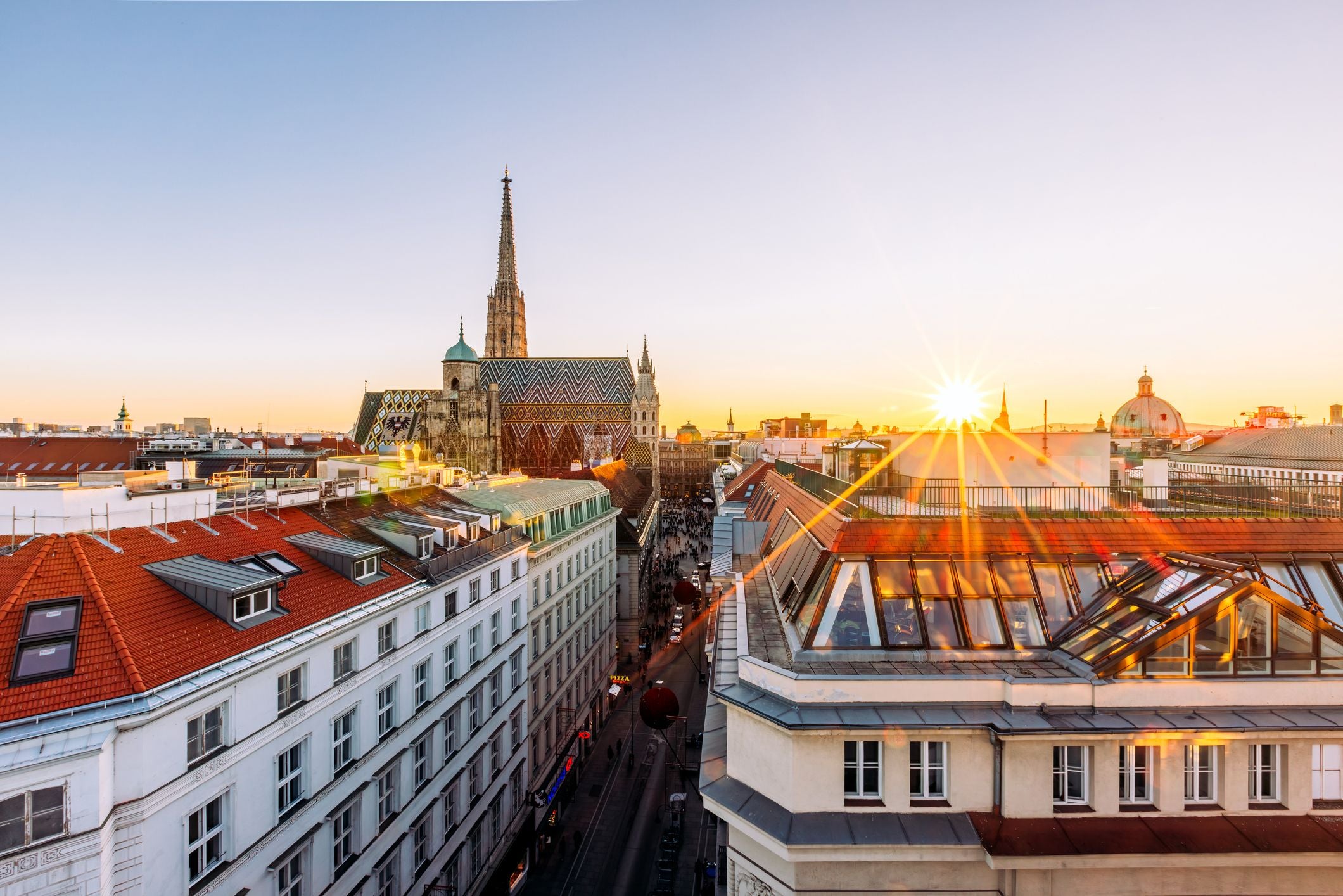 Blick auf Wien mit dem Stephansdom bei Sonnenuntergang und roten Dächern im Vordergrund.