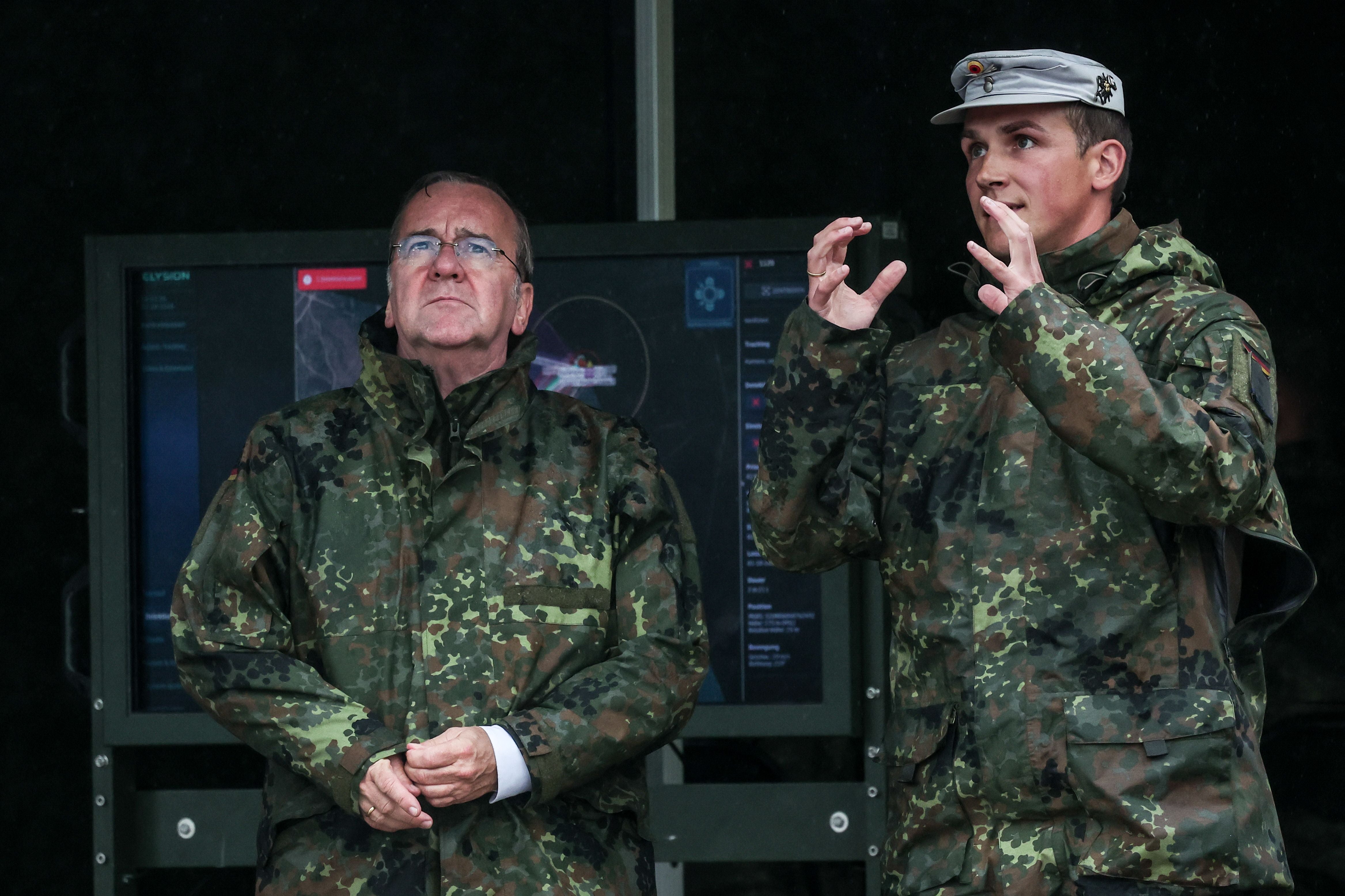 Zwei Männer in Bundeswehr-Uniformen stehen vor einem Monitor bei einer Militärübung.