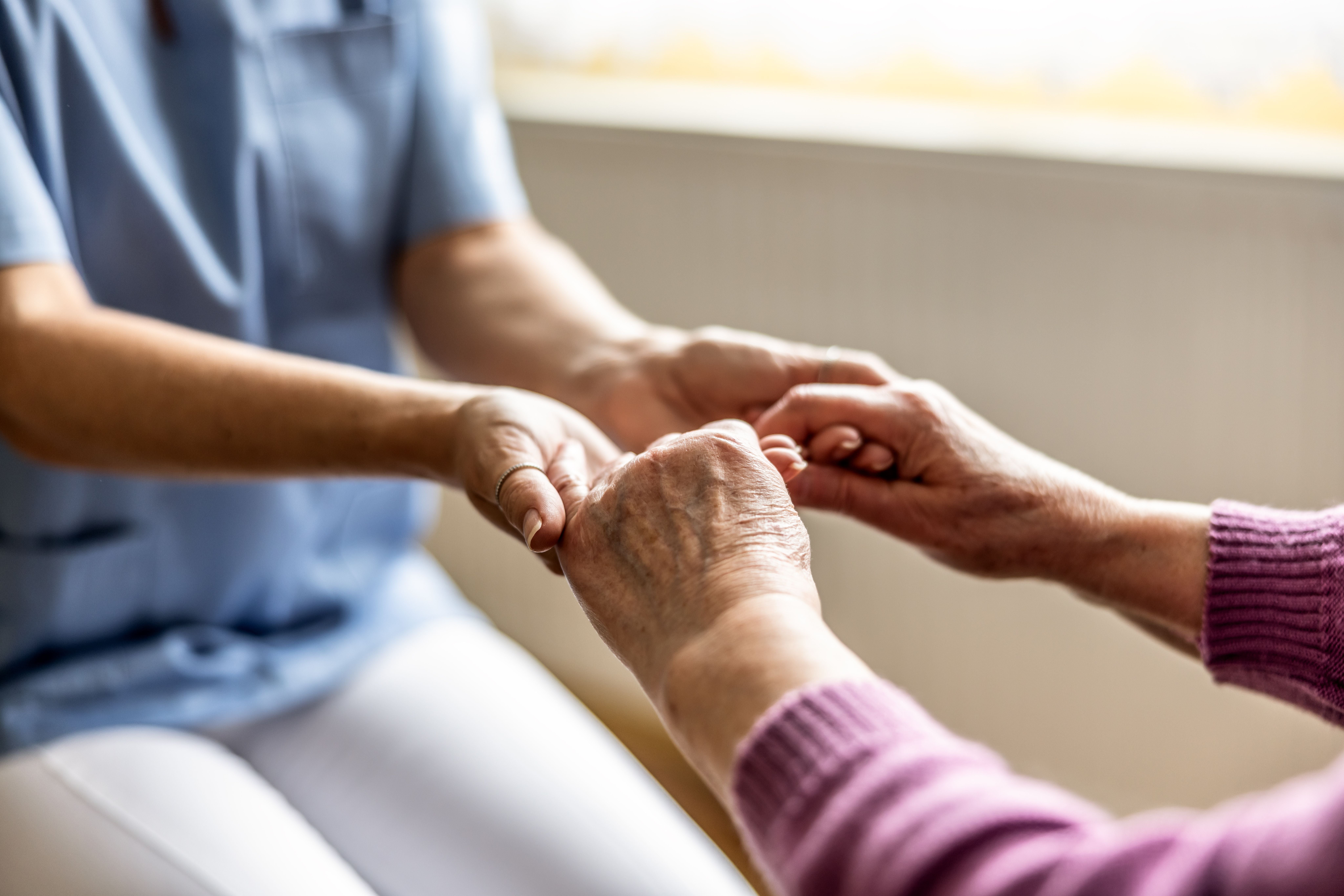 Nahaufnahme: Pflegerin hält fürsorglich die Hand einer älteren Person in einem Betreuungsumfeld.