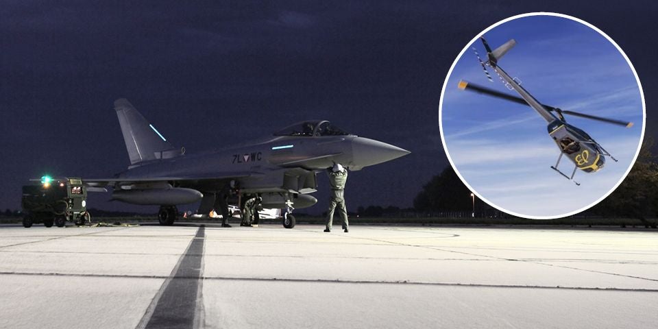 Eurofighter am Boden bei Nacht, oben rechts ein fliegender Hubschrauber Robinson R44.