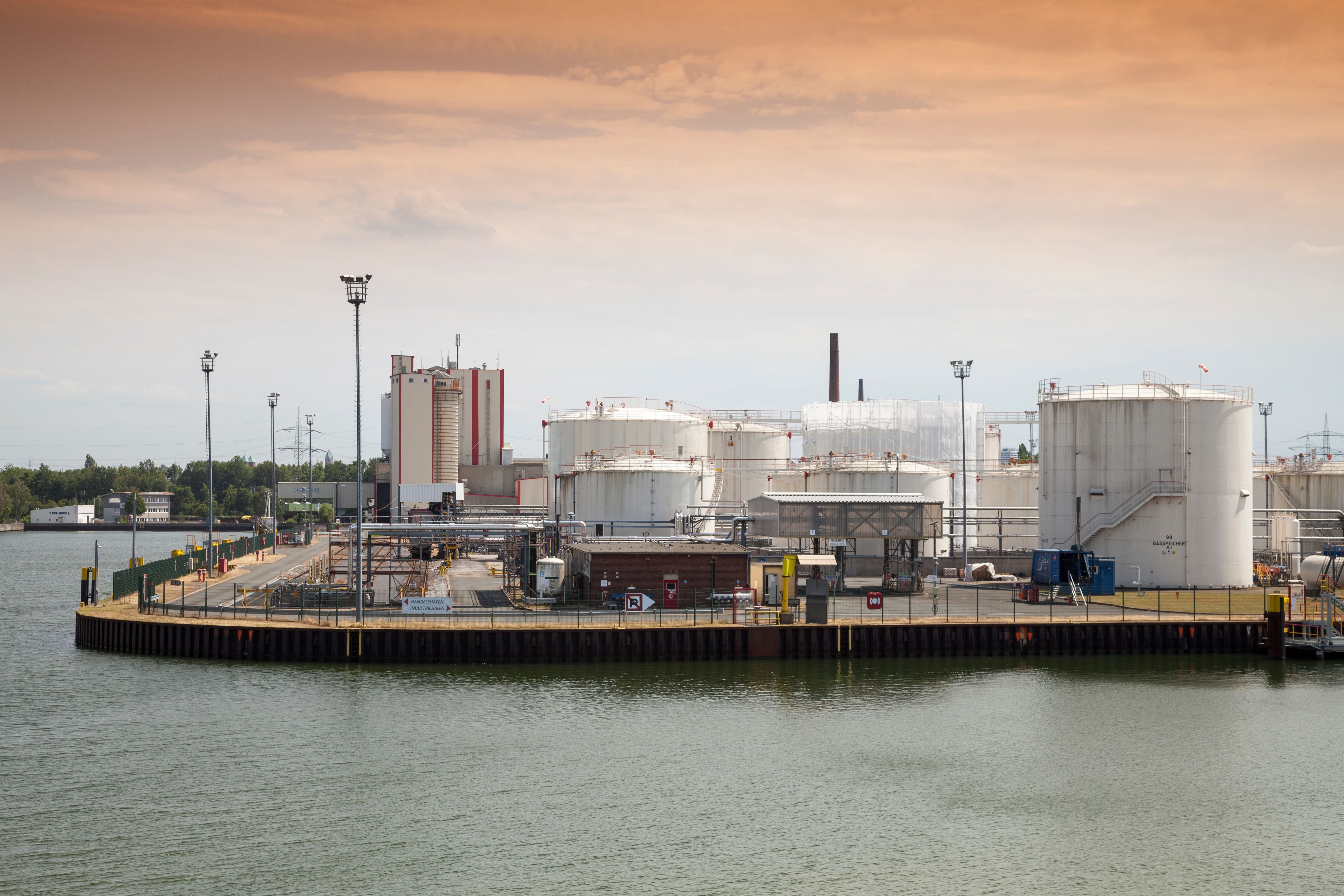Industriegelände mit großen Tanks am Wasser unter orangefarbenem Himmel bei Tageslicht.