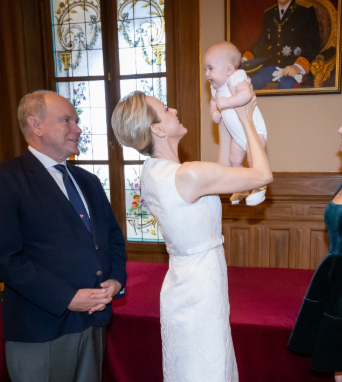 Eine Frau hebt ein lächelndes Baby hoch, ein Mann steht daneben und schaut zu.