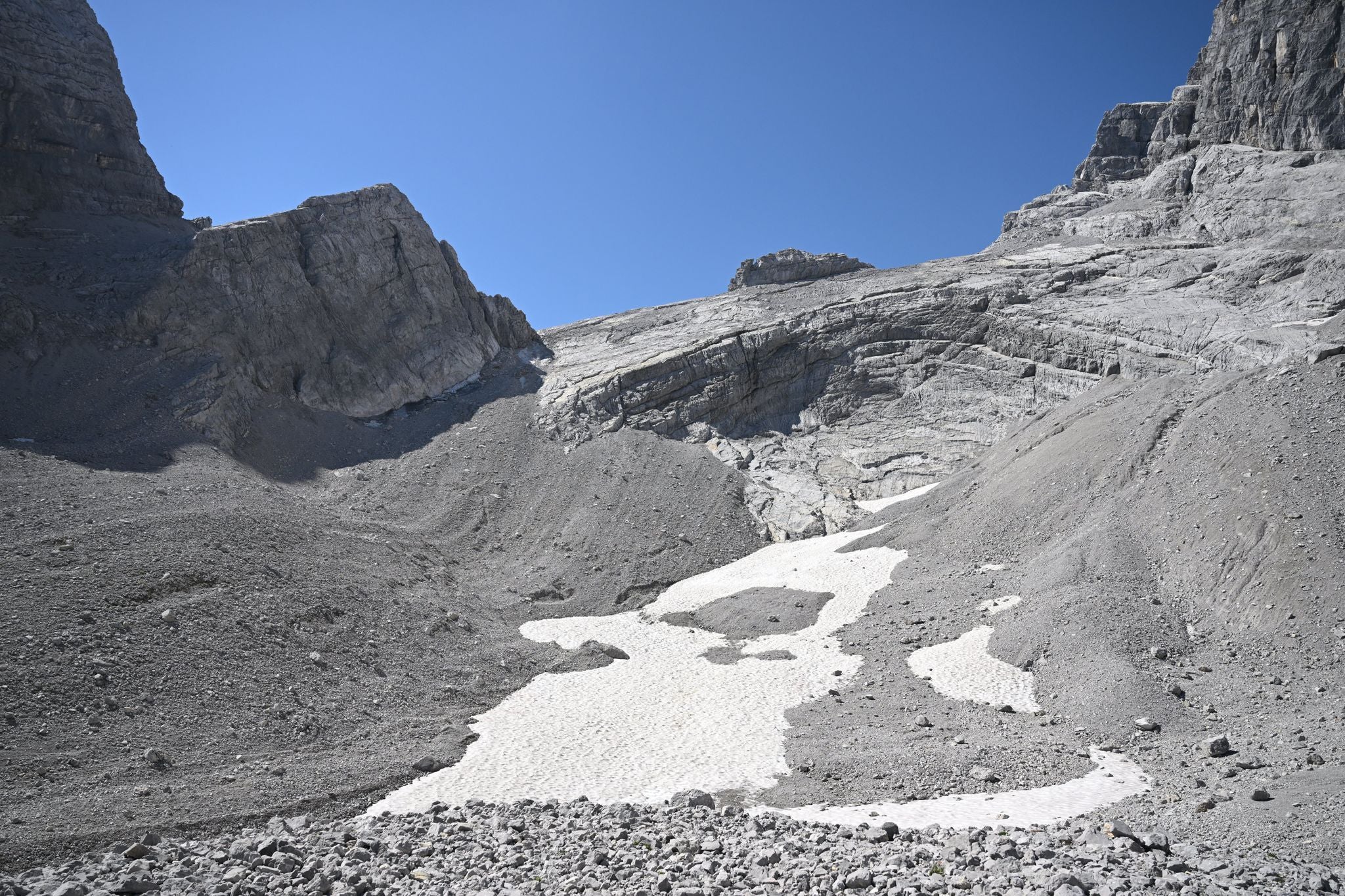 Schneerest auf dem Watzmanngletscher zwischen grauen Felsen unter blauem Himmel in Berchtesgaden.