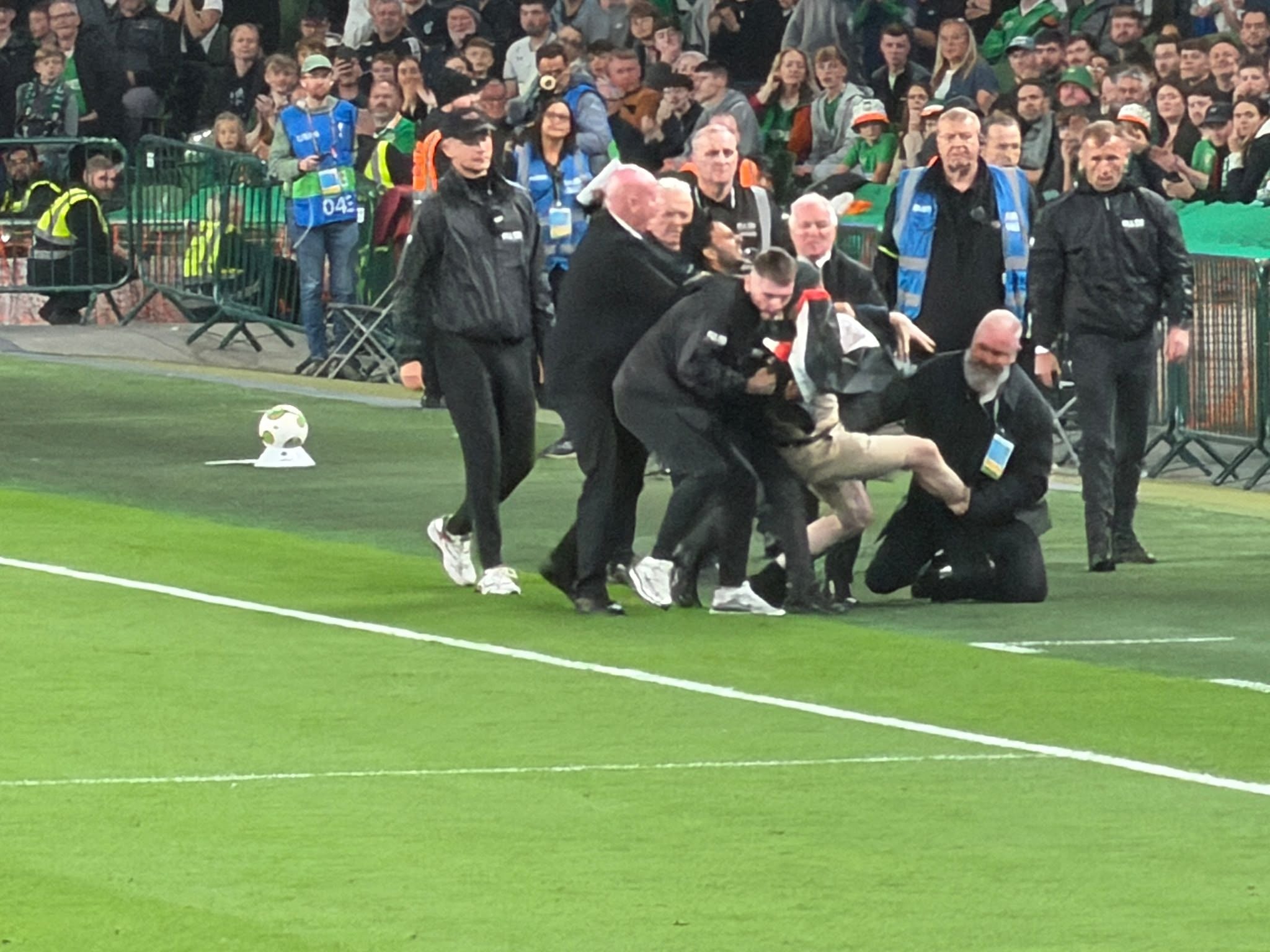Security-Personal hält eine Person am Spielfeldrand eines Fußballstadions fest.