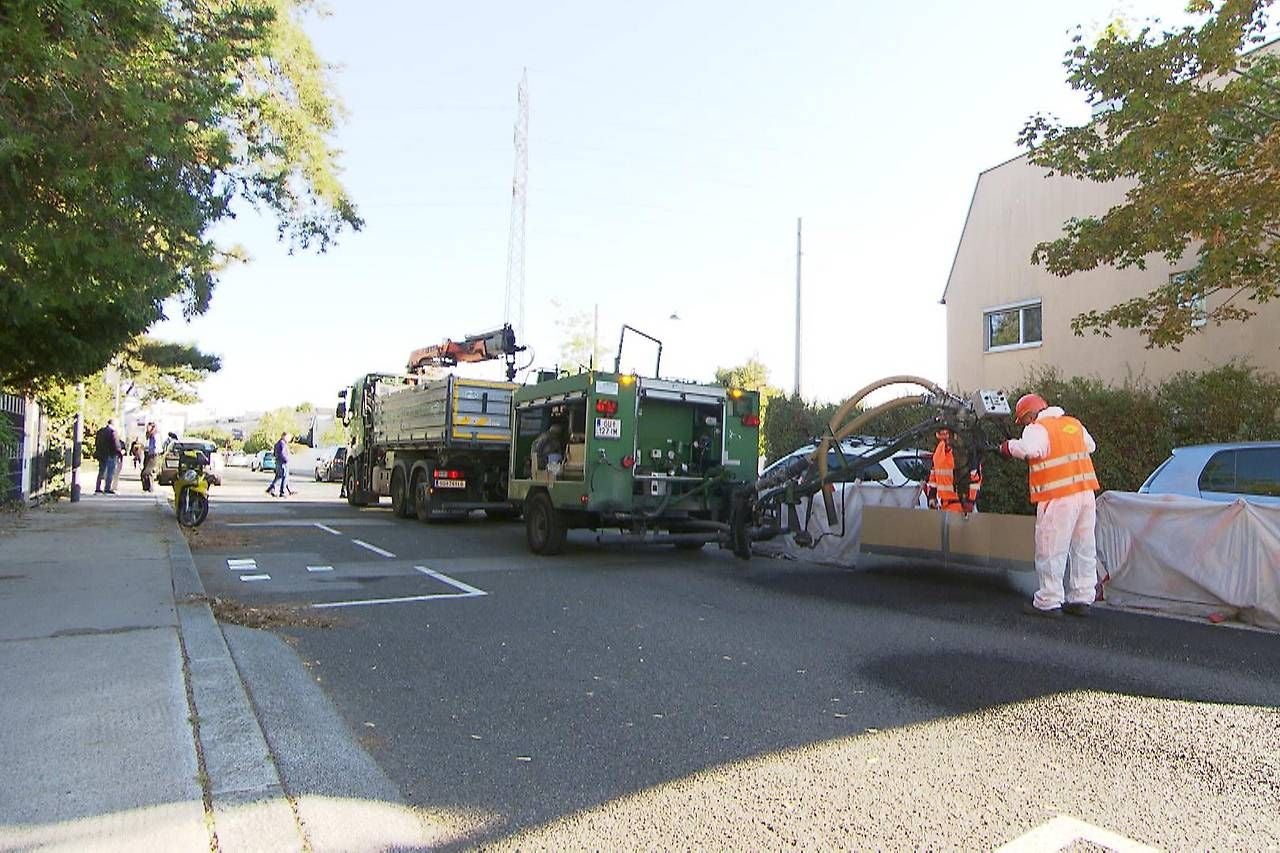 Arbeiter in Schutzkleidung führen Asbestsanierung an einer Straße mit Spezialfahrzeugen durch.